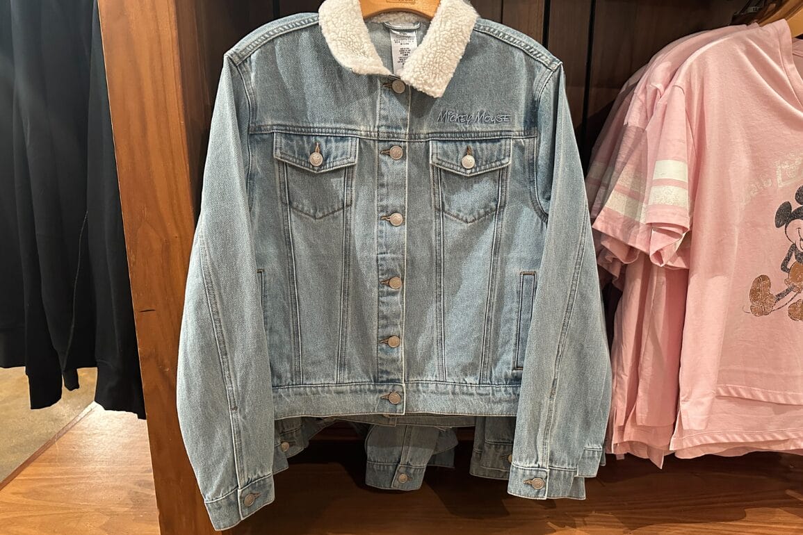 Light blue Mickey Denim Jacket with white sherpa collar beside a pink Walt Disney World Mickey Mouse shirt on a rack.