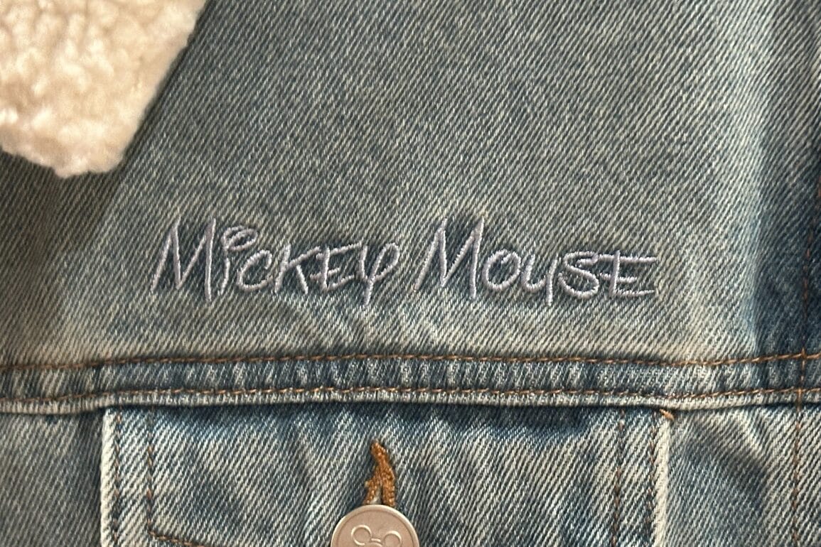 Close-up of Mickey Denim Jacket pocket with "Mickey Mouse" embroidered above it in white at Walt Disney World.