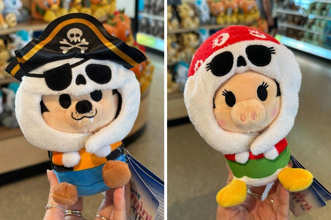 Two plush toys, Goofy and Clarabelle in pirate outfits, are held up in a Walt Disney World toy store.