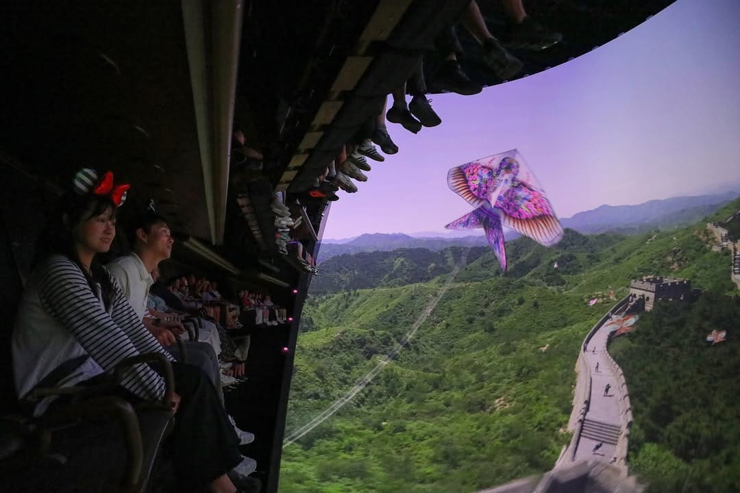 People on Shanghai Disney's Soaring Over the Horizon ride watch the Great Wall of China and a colorful kite on a big screen.