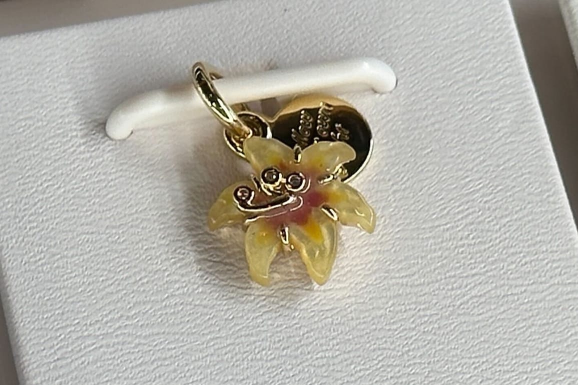 Close up of yellow and gold sundrop flower charm with gold "Follow Your Own Light" tag from Pandora's Tangled collection.