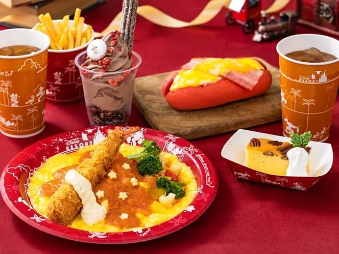 A festive meal at Tokyo Disneyland with omelette rice, shrimp, fries, soup, dessert cup, and drinks on a red table.