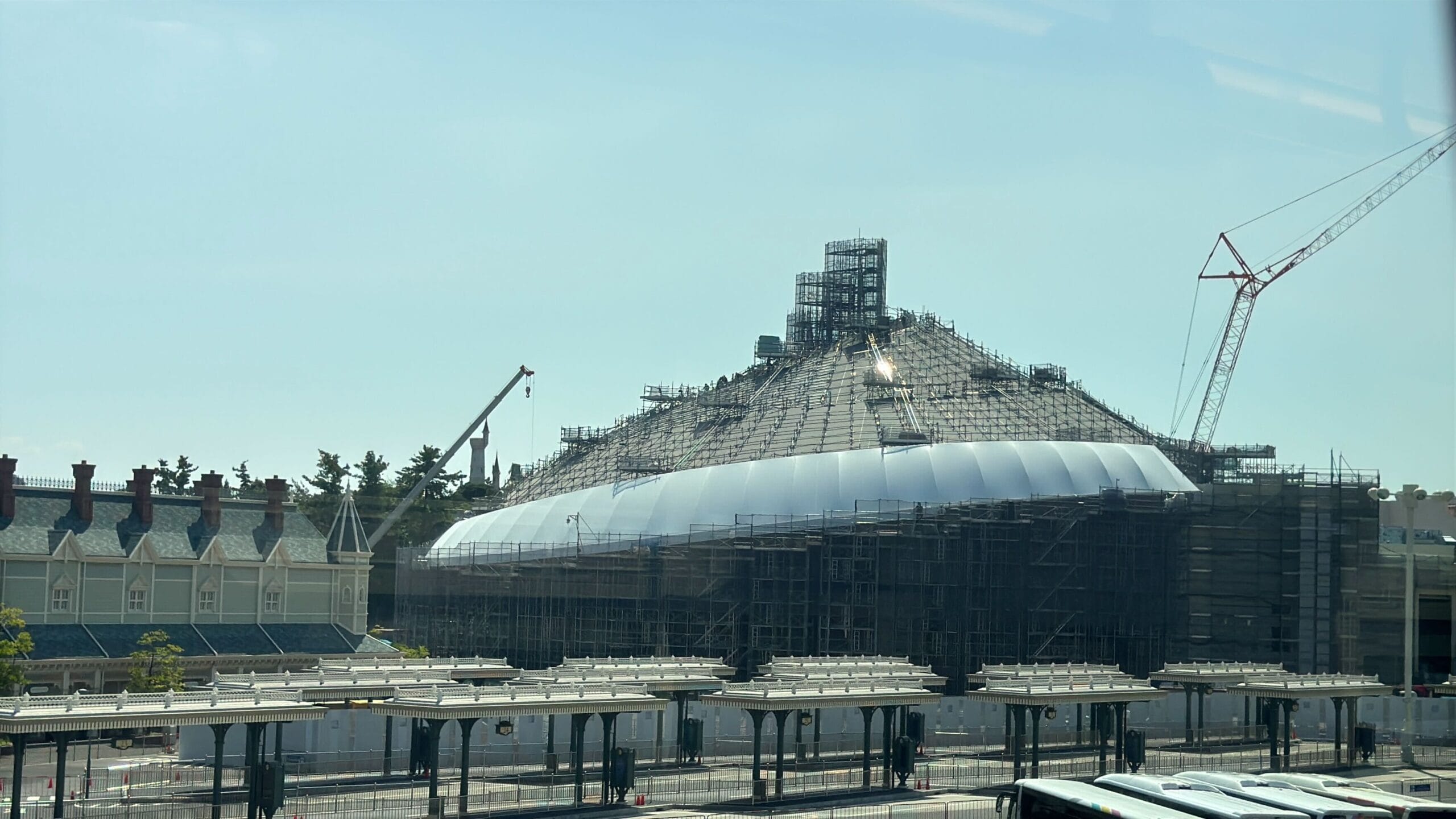 Large dome-shaped building under construction with scaffolding and cranes surrounding it on a sunny day.