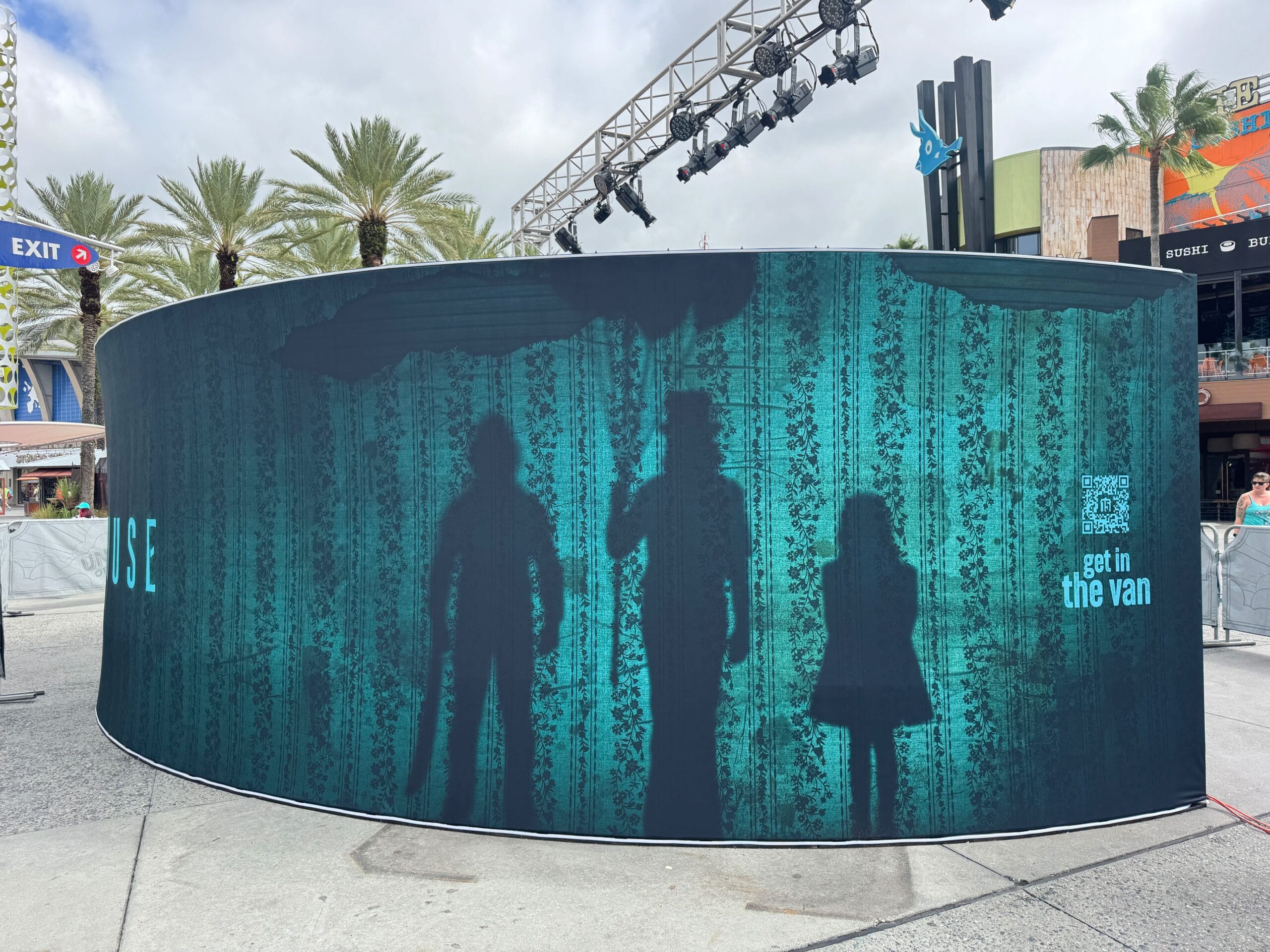 Curved wall with three blue silhouettes: two adults and a child, under palm trees, at an outdoor public area.