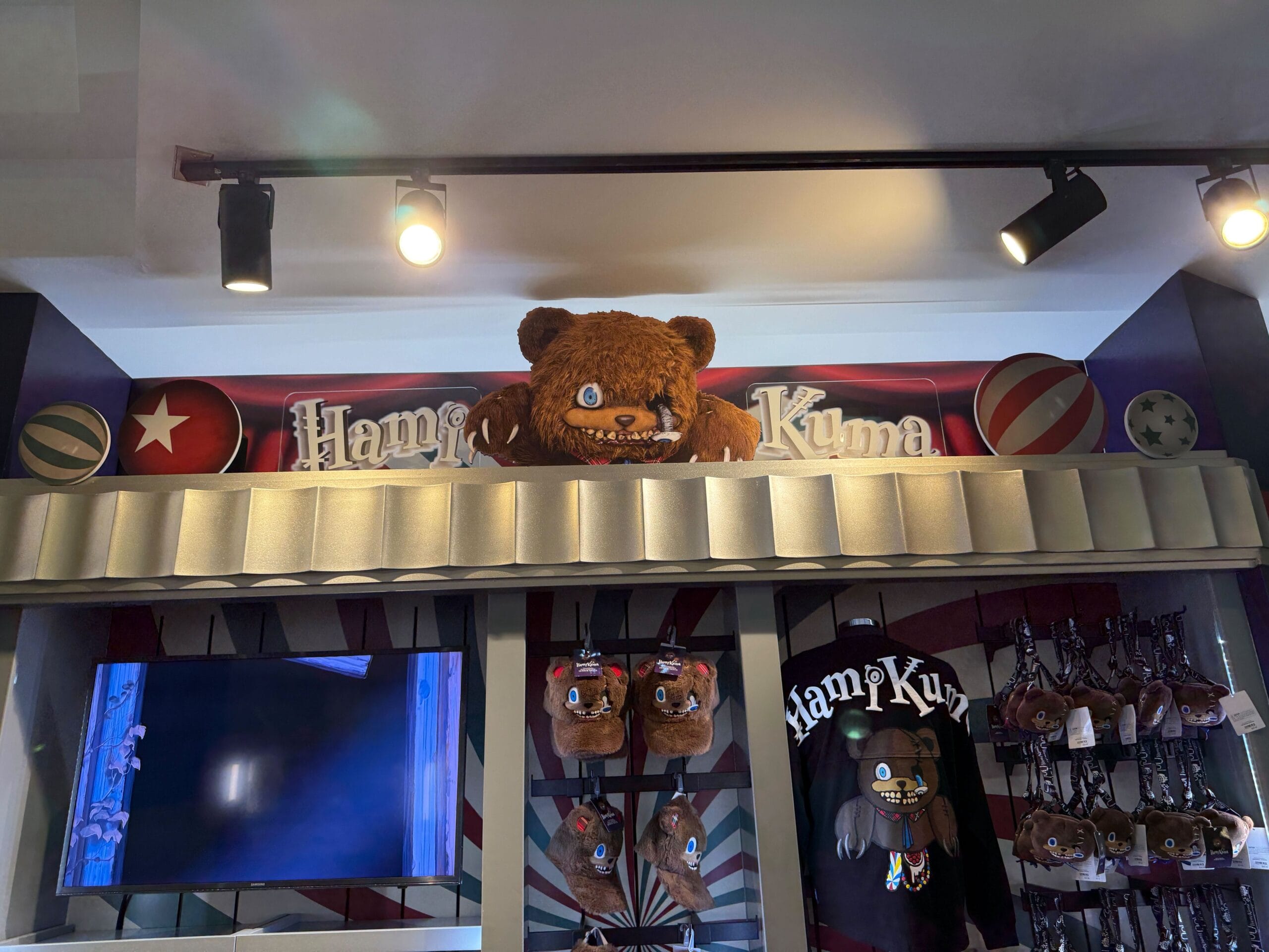 Large brown teddy bear with sharp teeth above HamiKuma Merchandise display at Universal Orlando Resort gift shop.