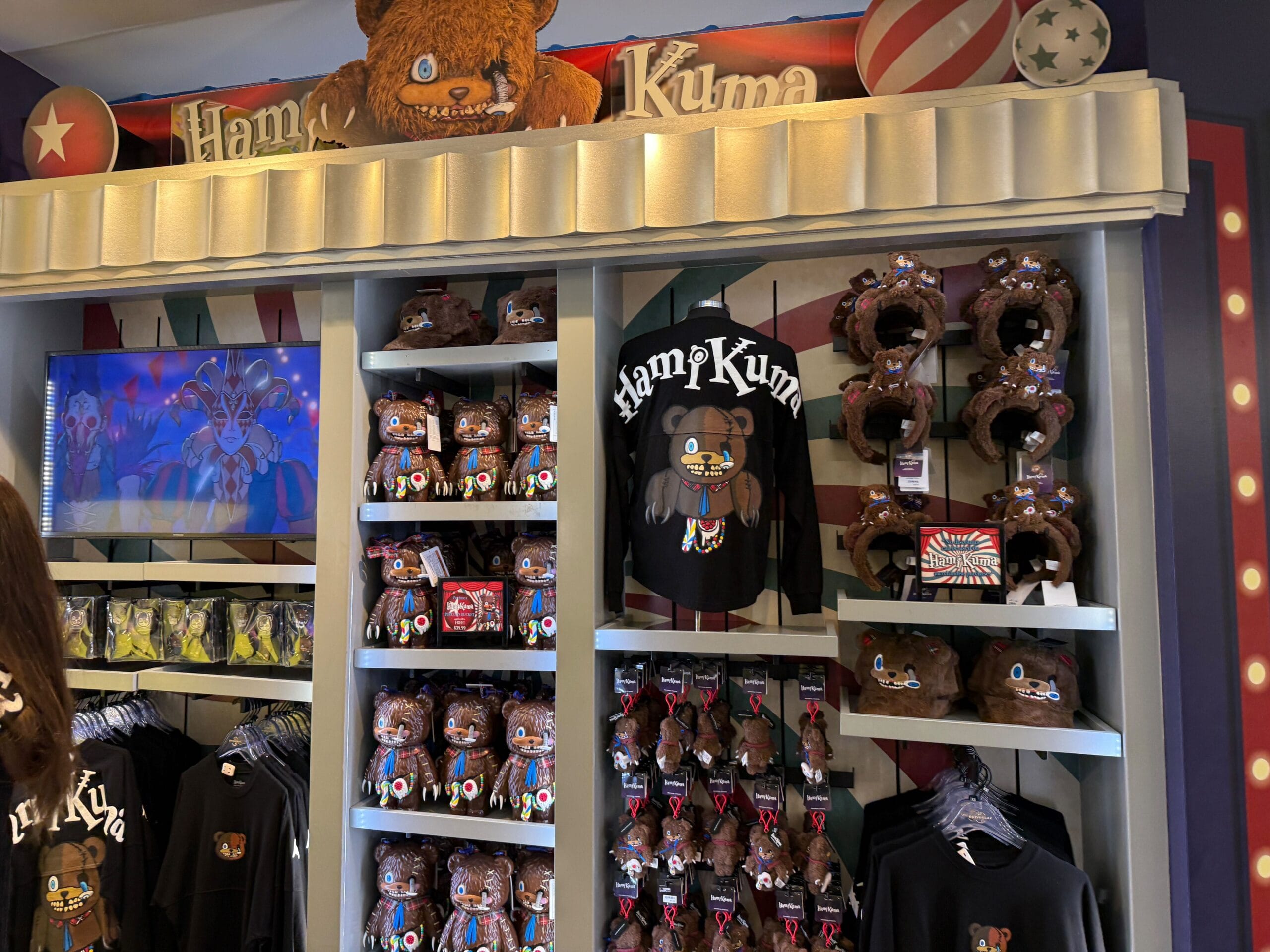 Store display with plush toys, hats, and shirts featuring a brown bear character named HamKuma in a colorful setting.