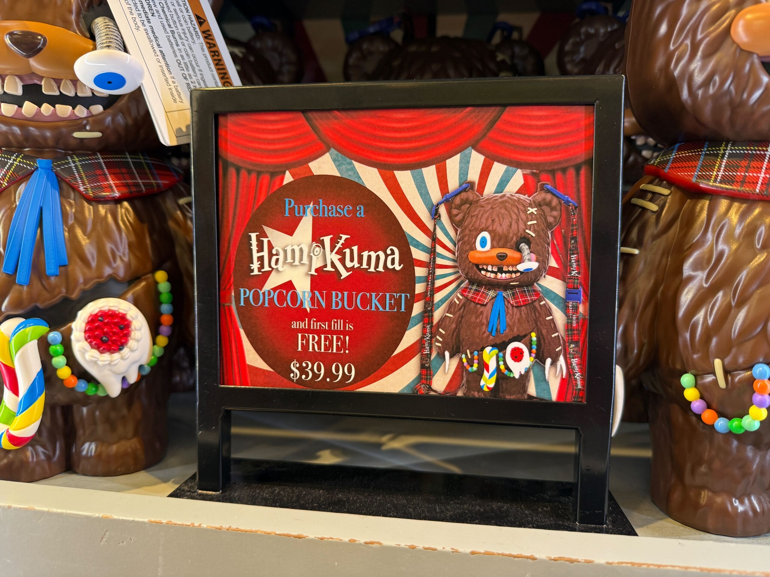Sign advertising a Hamikuma popcorn bucket with first fill free for $39.99, surrounded by bear figures.