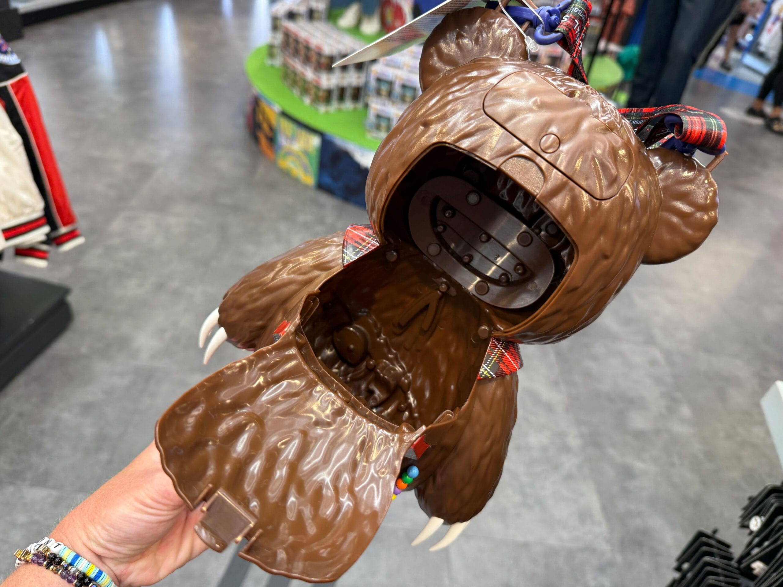 A hand holds open a bear-shaped plastic purse with a plaid interior in a store.