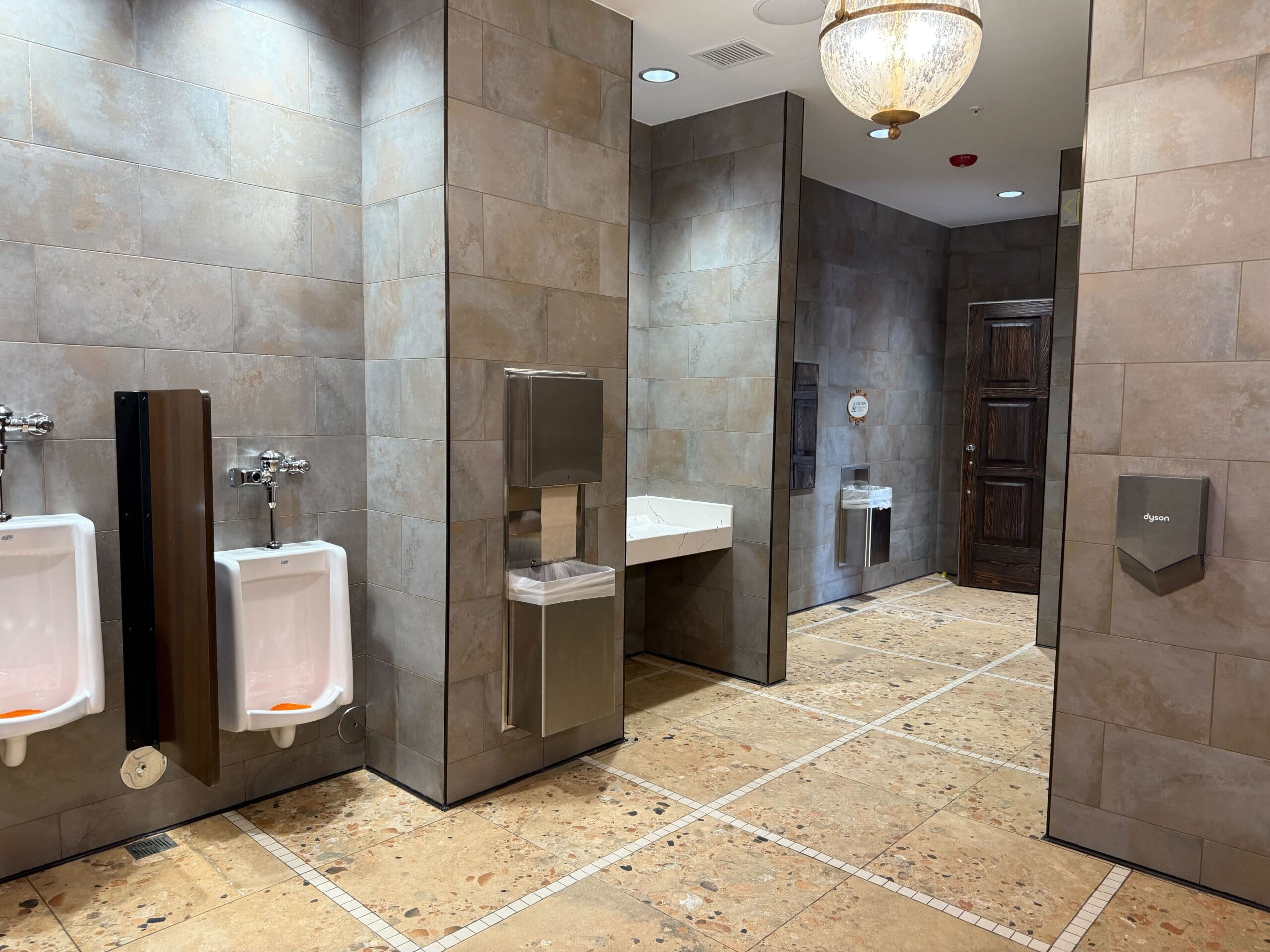 A clean Port of Entry Restrooms at Universal Islands of Adventure with urinals, sinks, and beige tiled walls and floors.