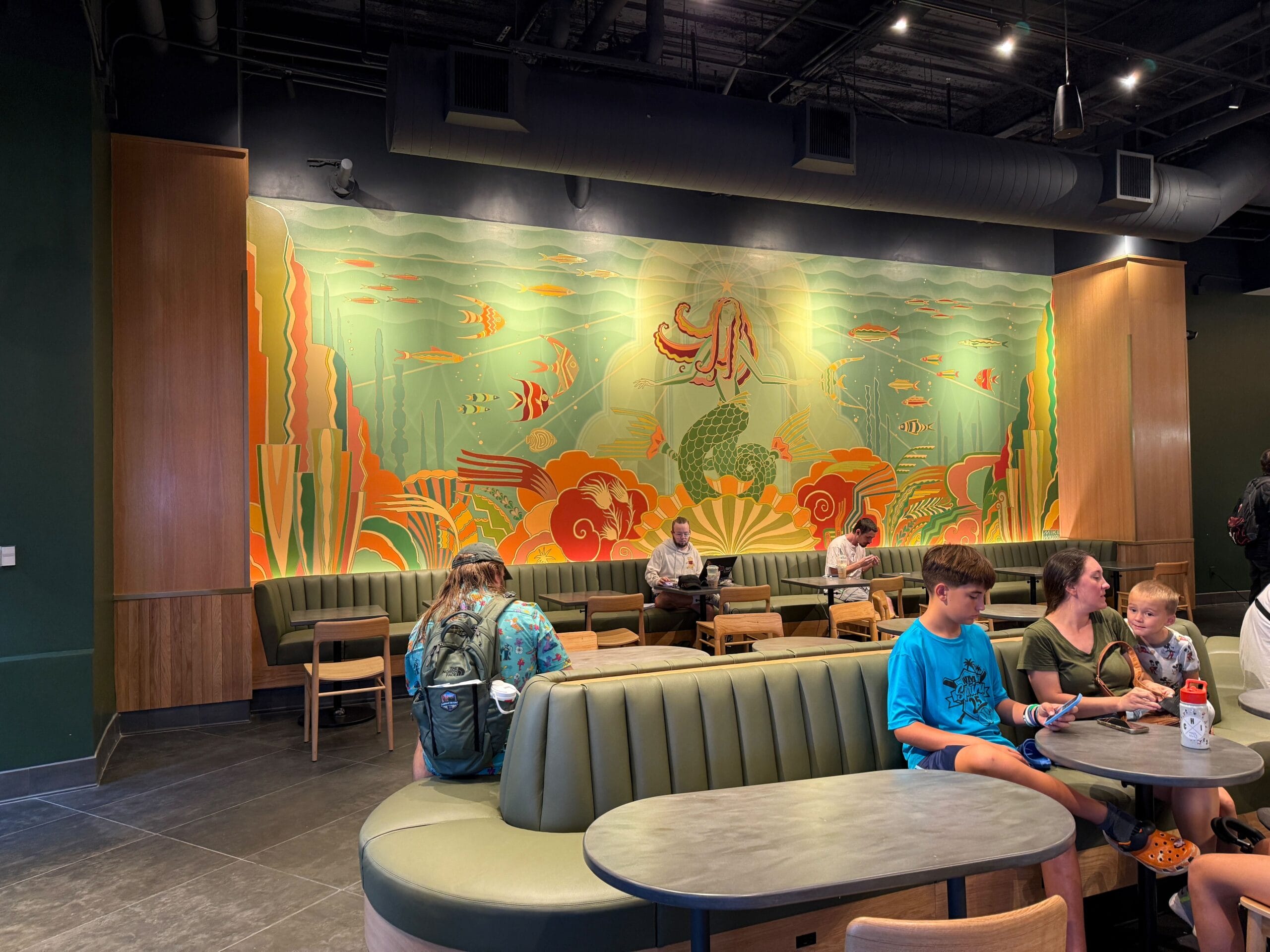 People sitting in a cafe with green booths and an underwater-themed mural at Universal Orlando’s CityWalk.