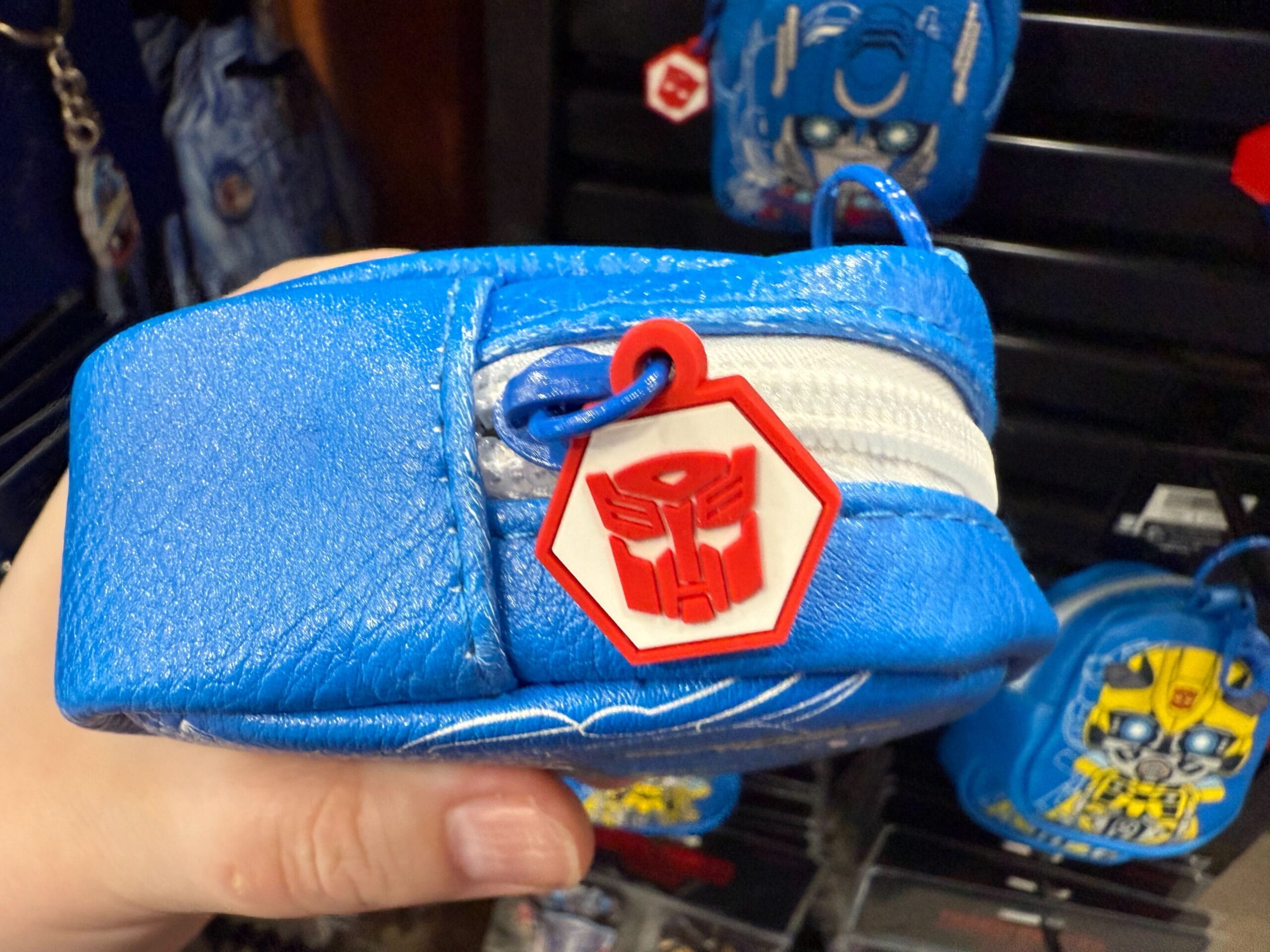 A hand holds a blue Transformers pouch with a red Autobot logo zipper pull.