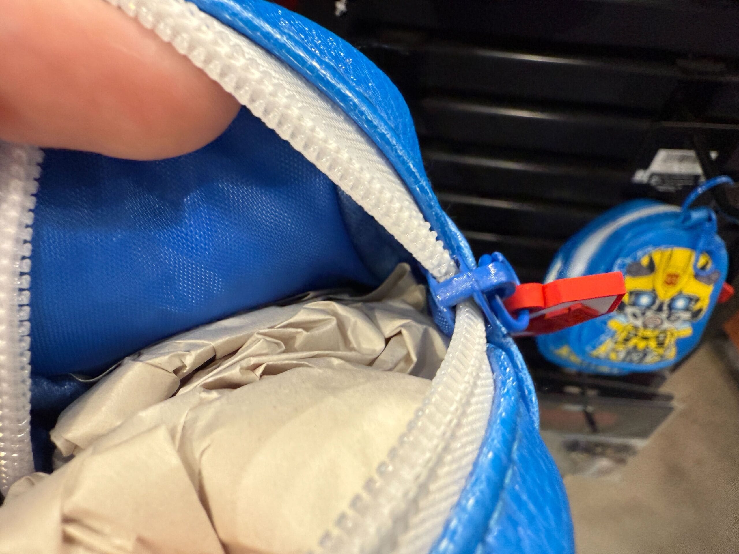 Close-up of a blue zippered pouch partially open, showing crumpled paper inside, with another pouch in the background.