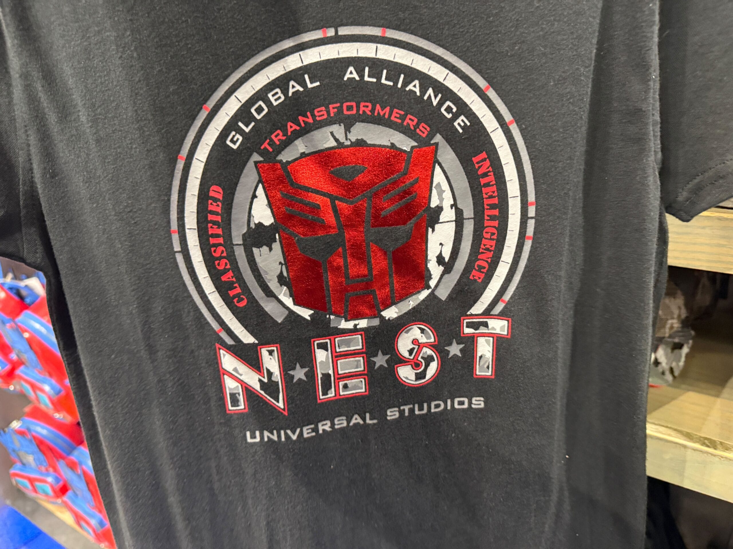 Black T-shirt with a red Transformers emblem and "NEST" logo, promoting Universal Studios.