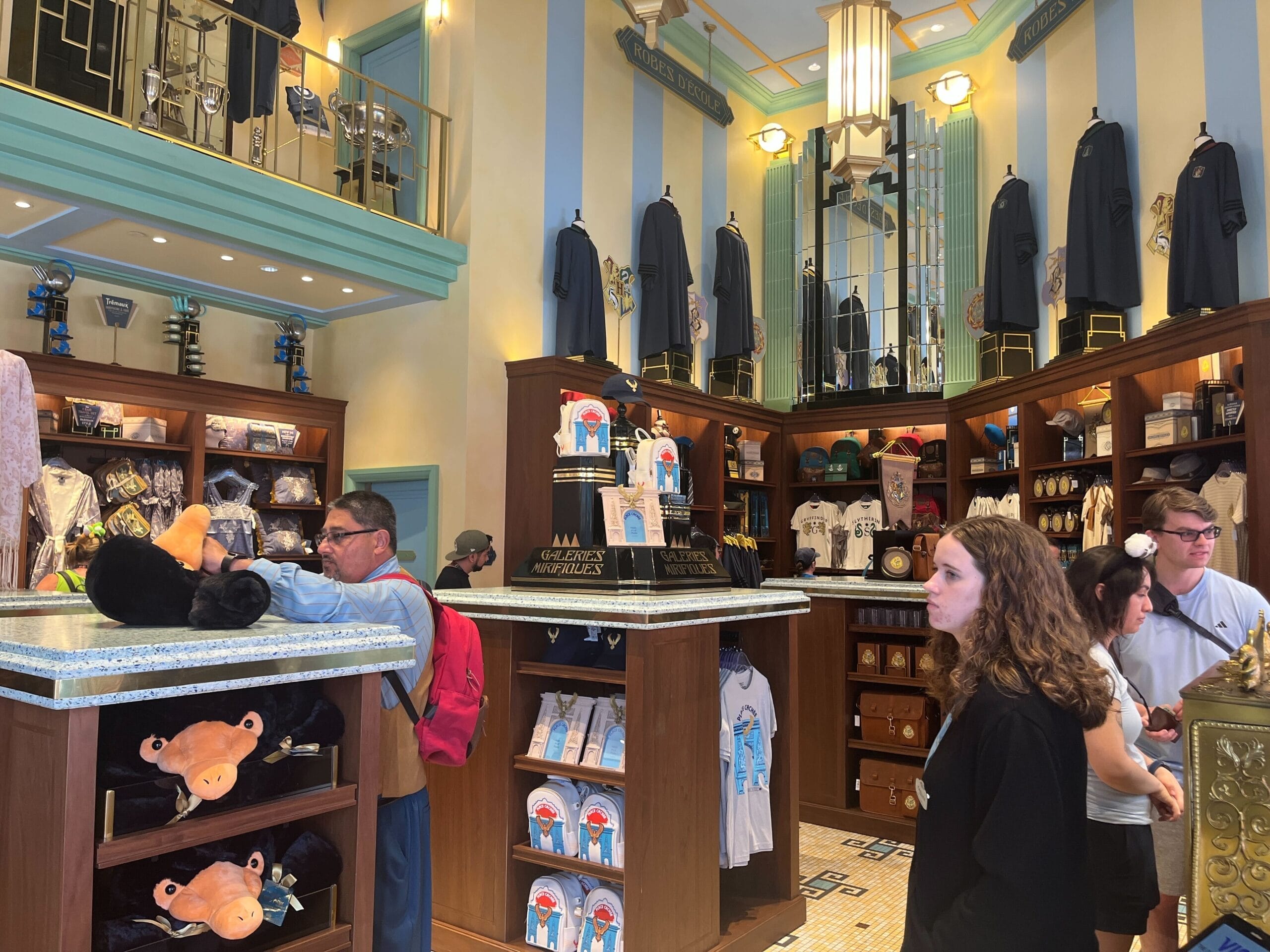 People browse plush toys and clothing in Les Galeries Mirifiques, a brightly lit souvenir shop with striped walls.