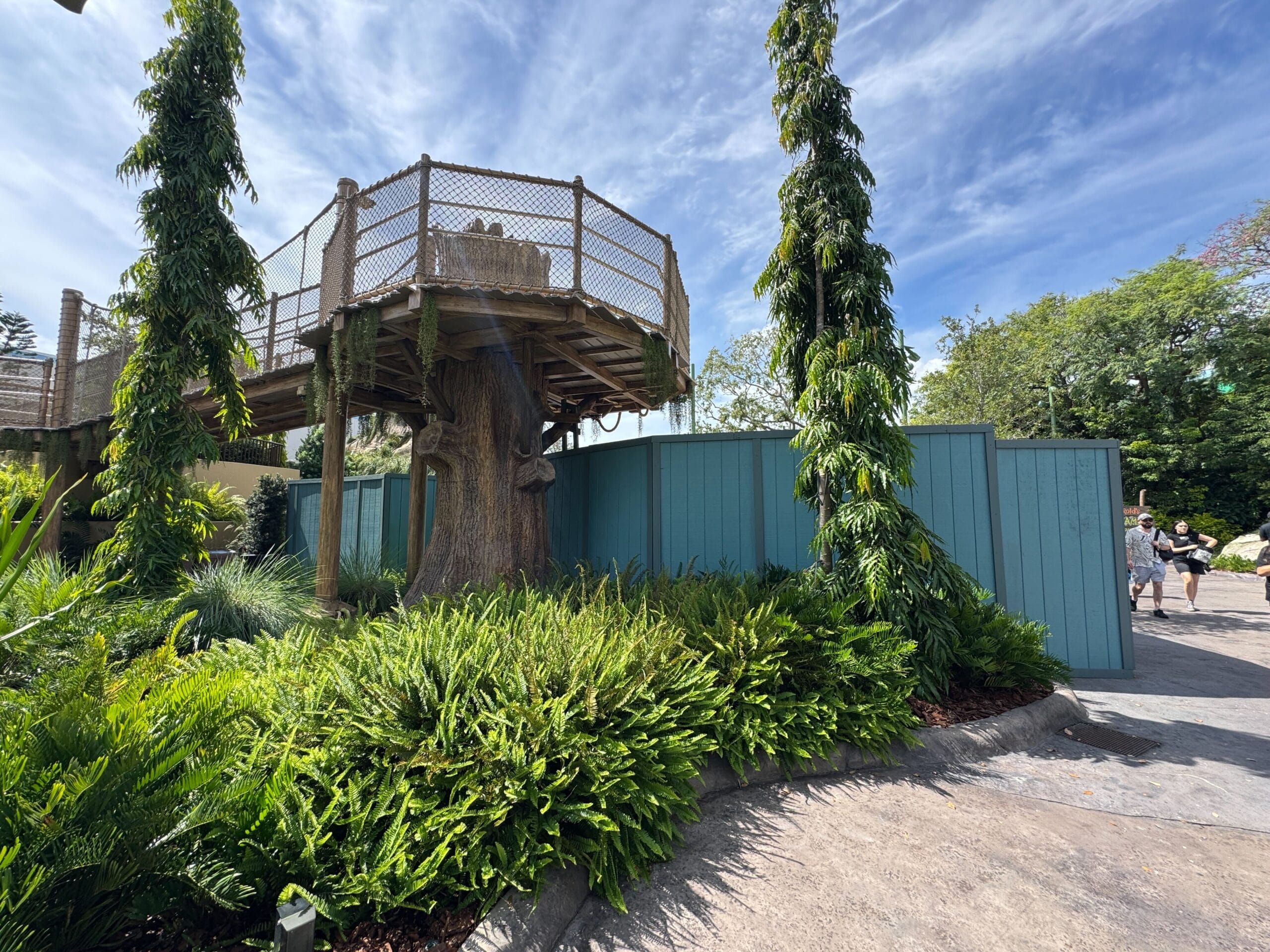 A wooden treehouse with railings overlooks greenery near a Swamp Splash Pad at Universal Studios Florida.