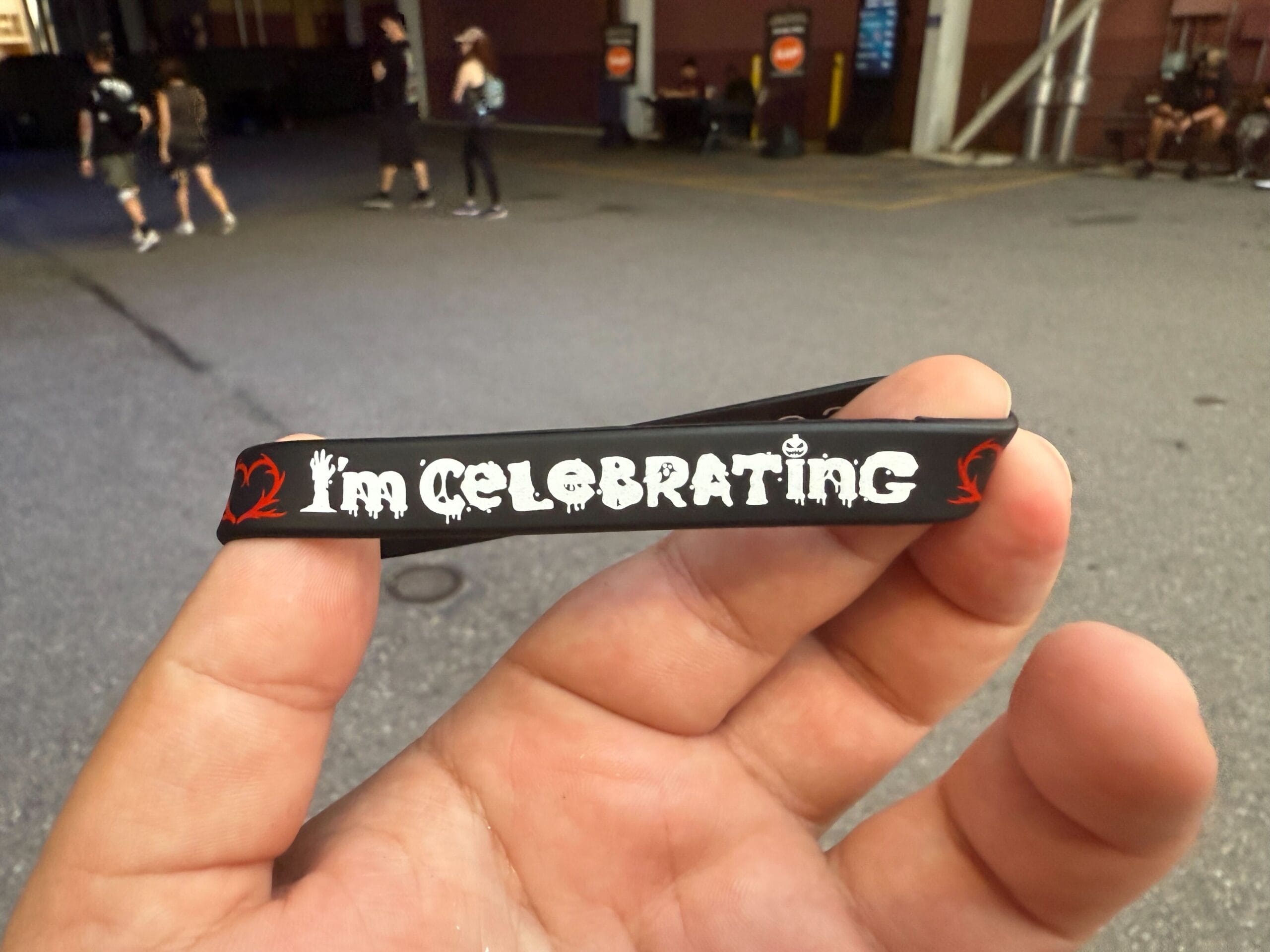 A hand holds a black wristband that reads "I'm CELEBRATING" in white letters with red accents.