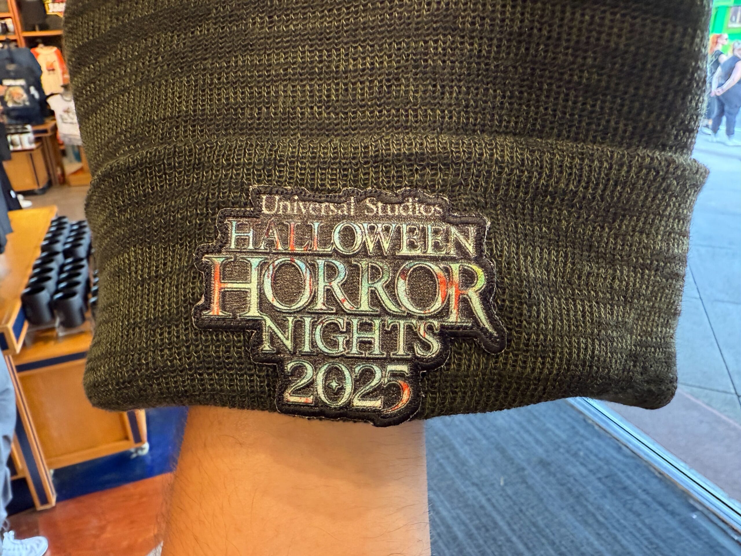 A green beanie featuring an embroidered "Halloween Horror Nights 2025" logo in a store.