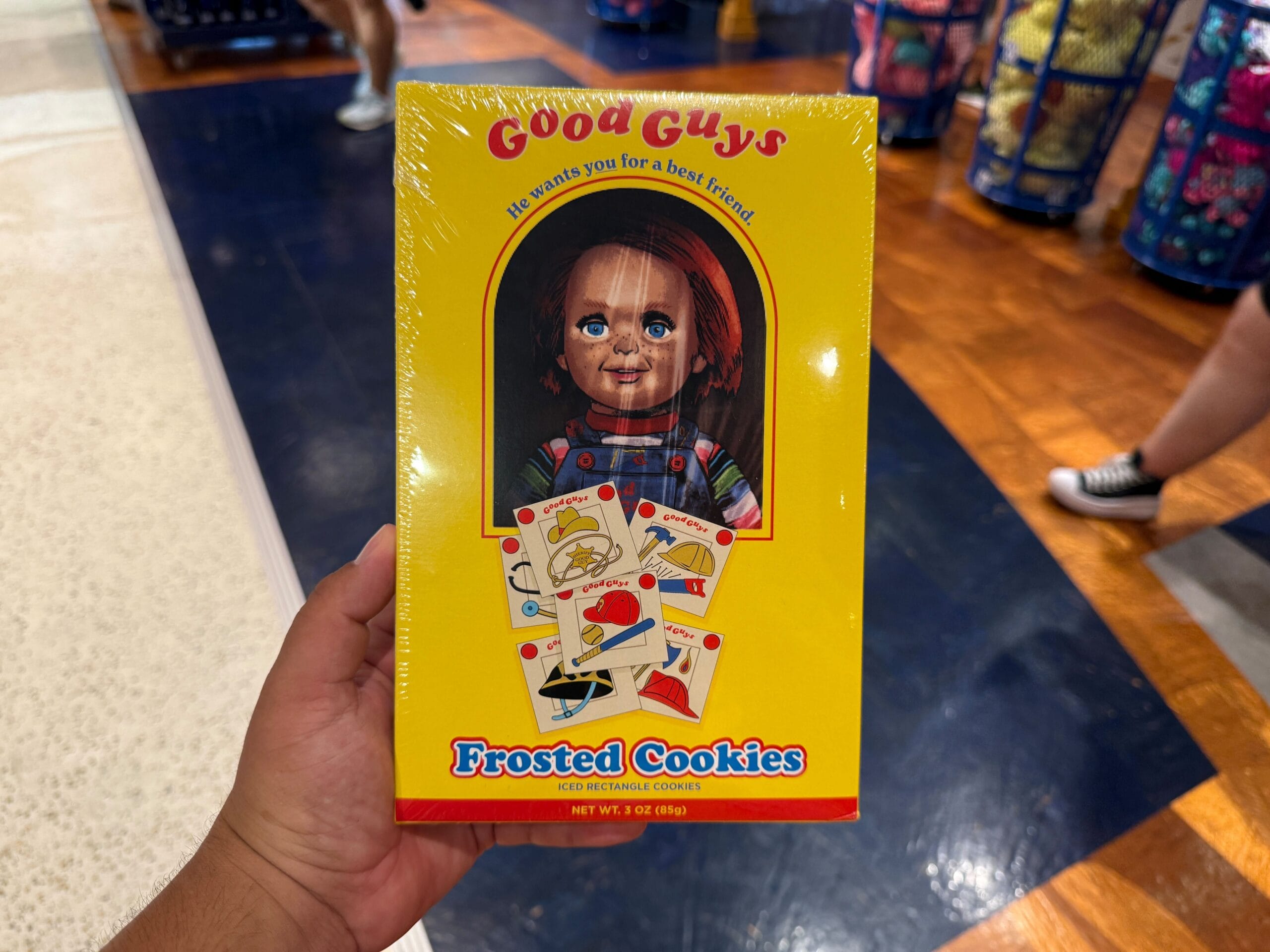 A hand holds a yellow Good Guys Frosted Cookies box featuring a doll with red hair and colorful cards on the front.