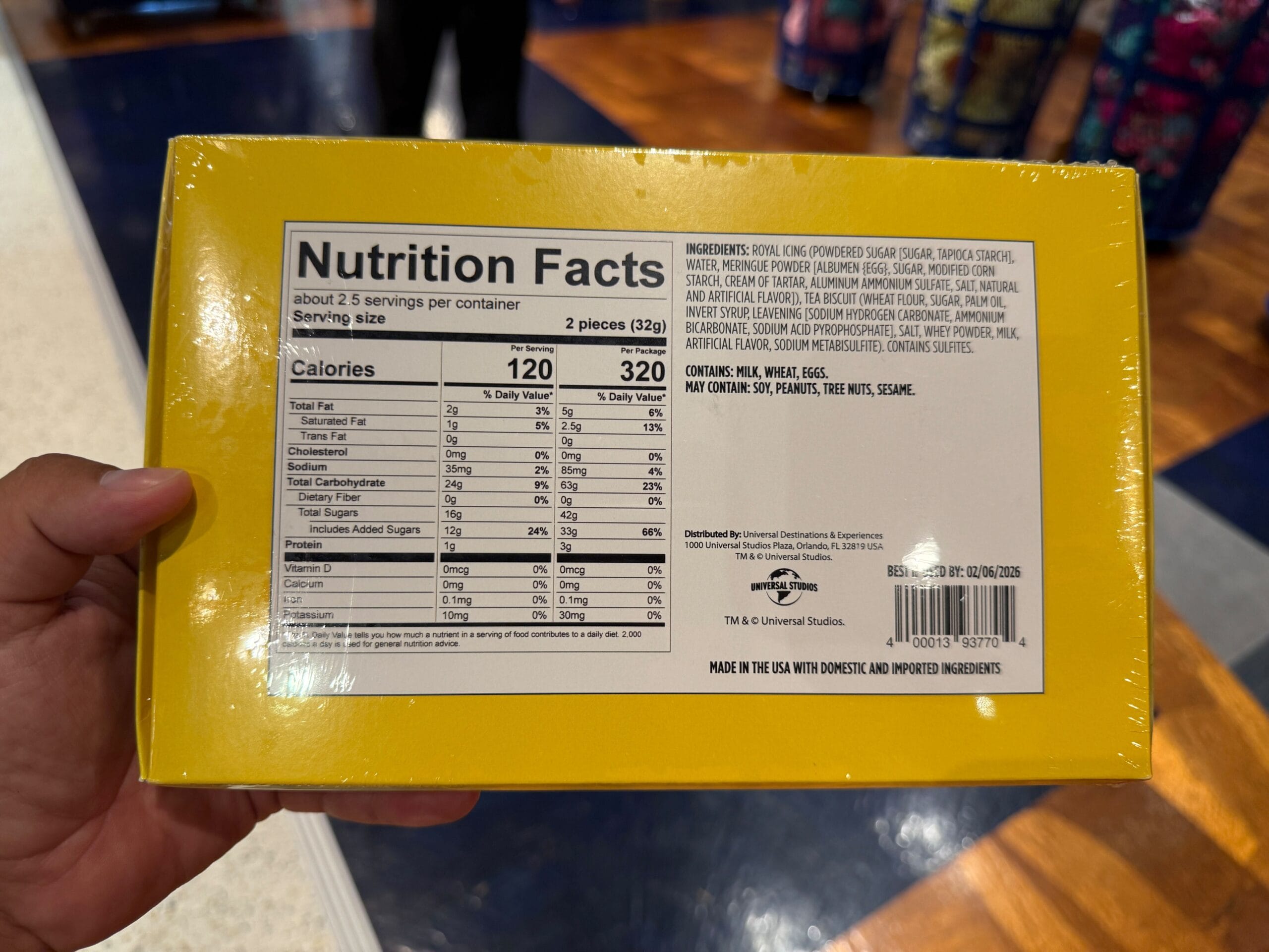 Hand holding a yellow box showing nutrition facts and ingredients label for a food product in a store.