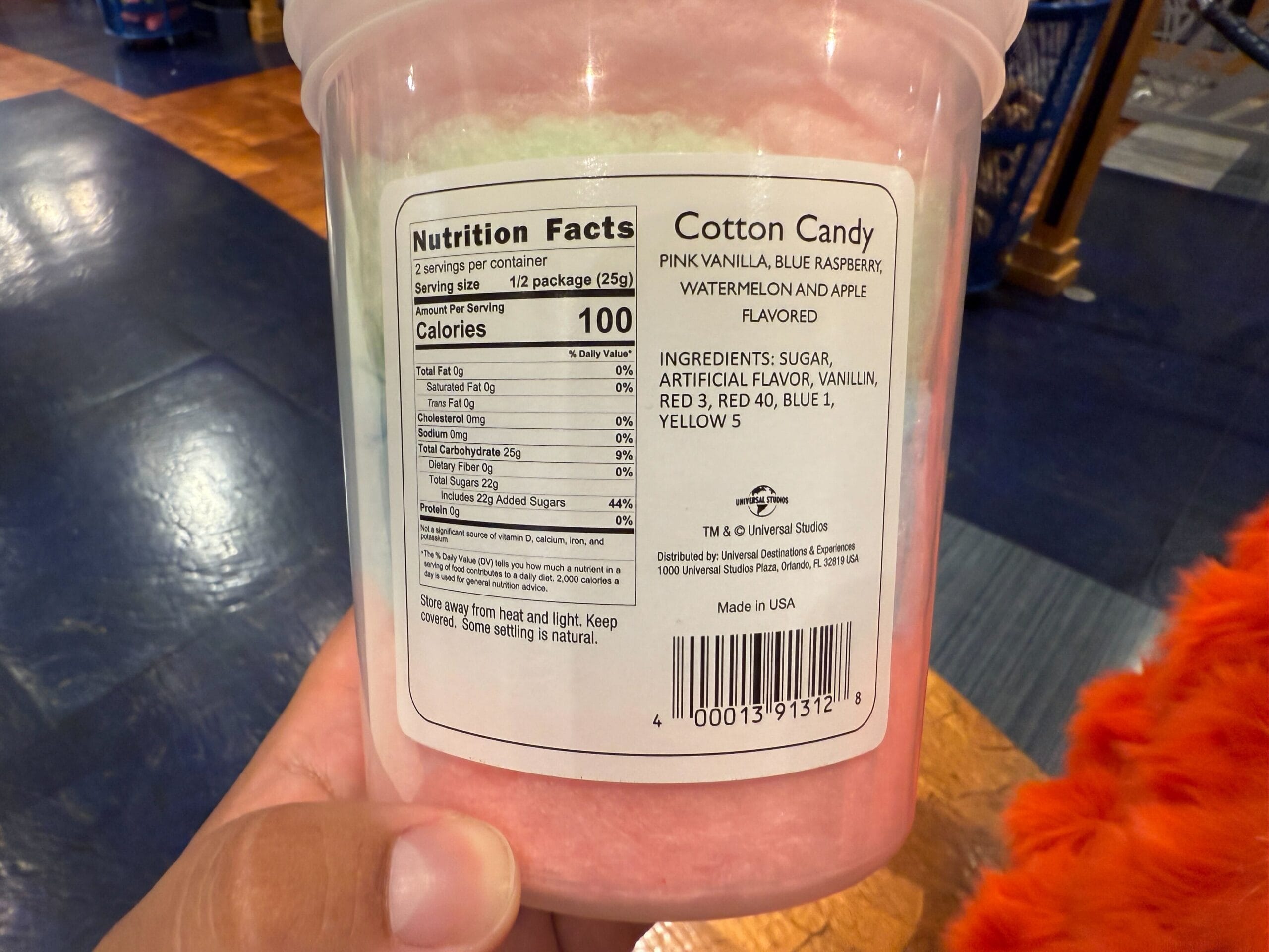 A hand holds a tub of cotton candy with nutrition facts and ingredients label visible.