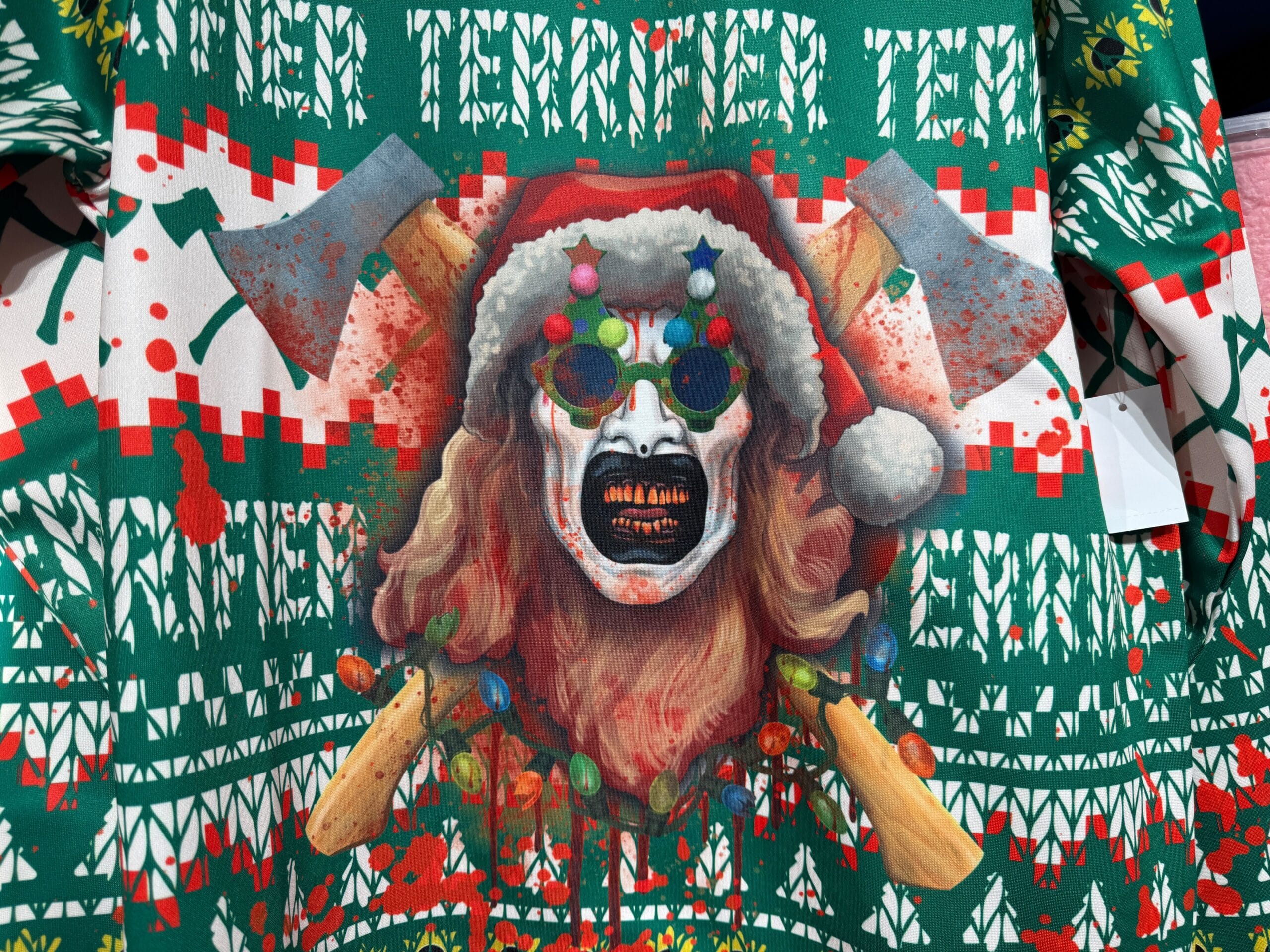 A creepy Santa face with sunglasses, axes, and Christmas lights on a green and red holiday sweater.