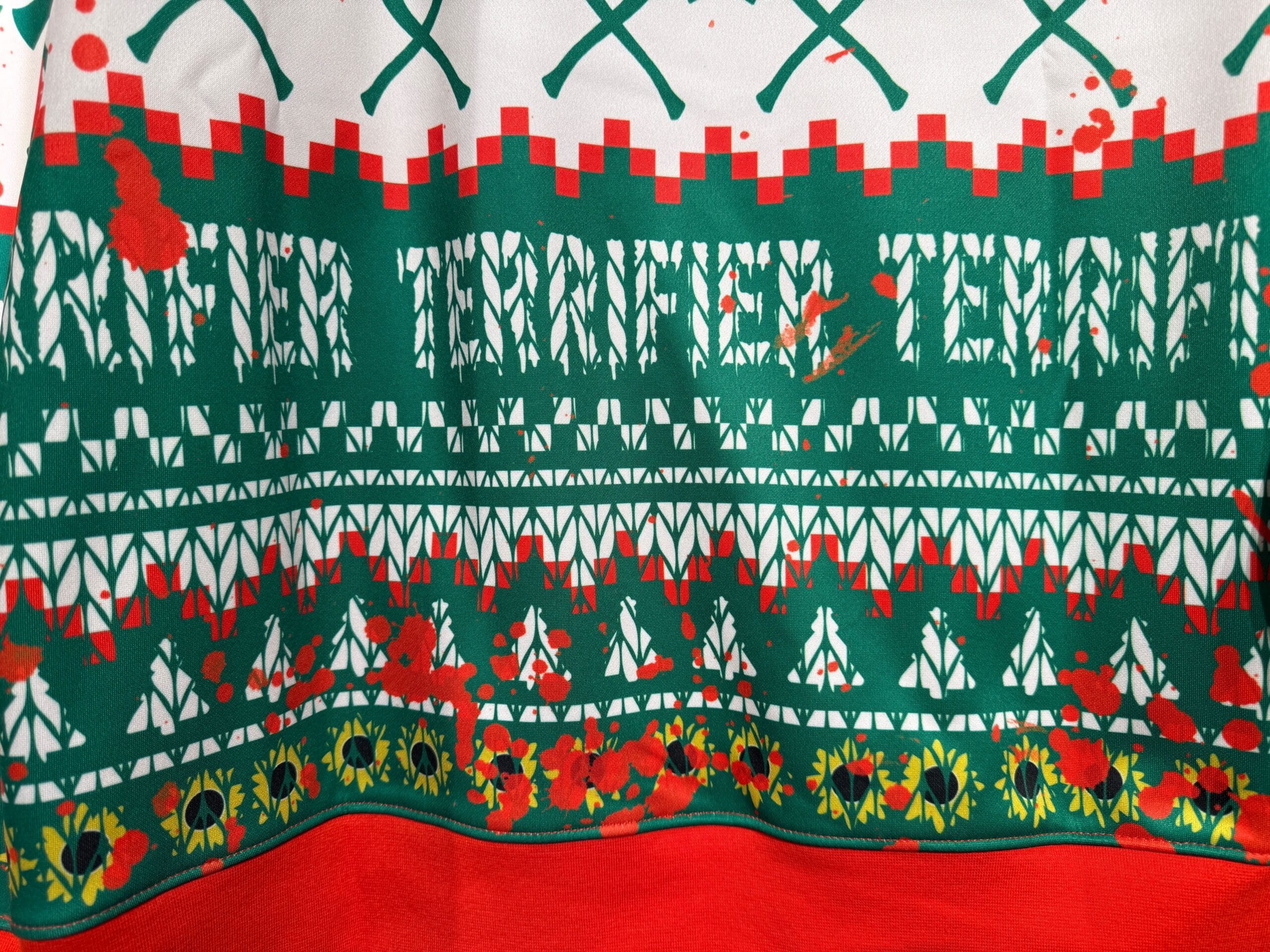 A patterned fabric with green, red, and white designs and red splatters resembling blood stains.
