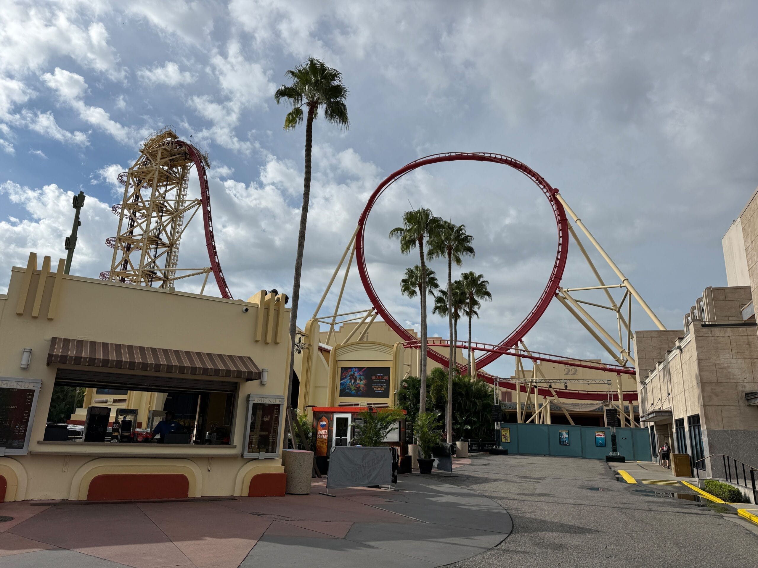 Red Rip Ride Rockit roller coaster with loops and palm trees under a cloudy sky at Universal Studios entrance.
