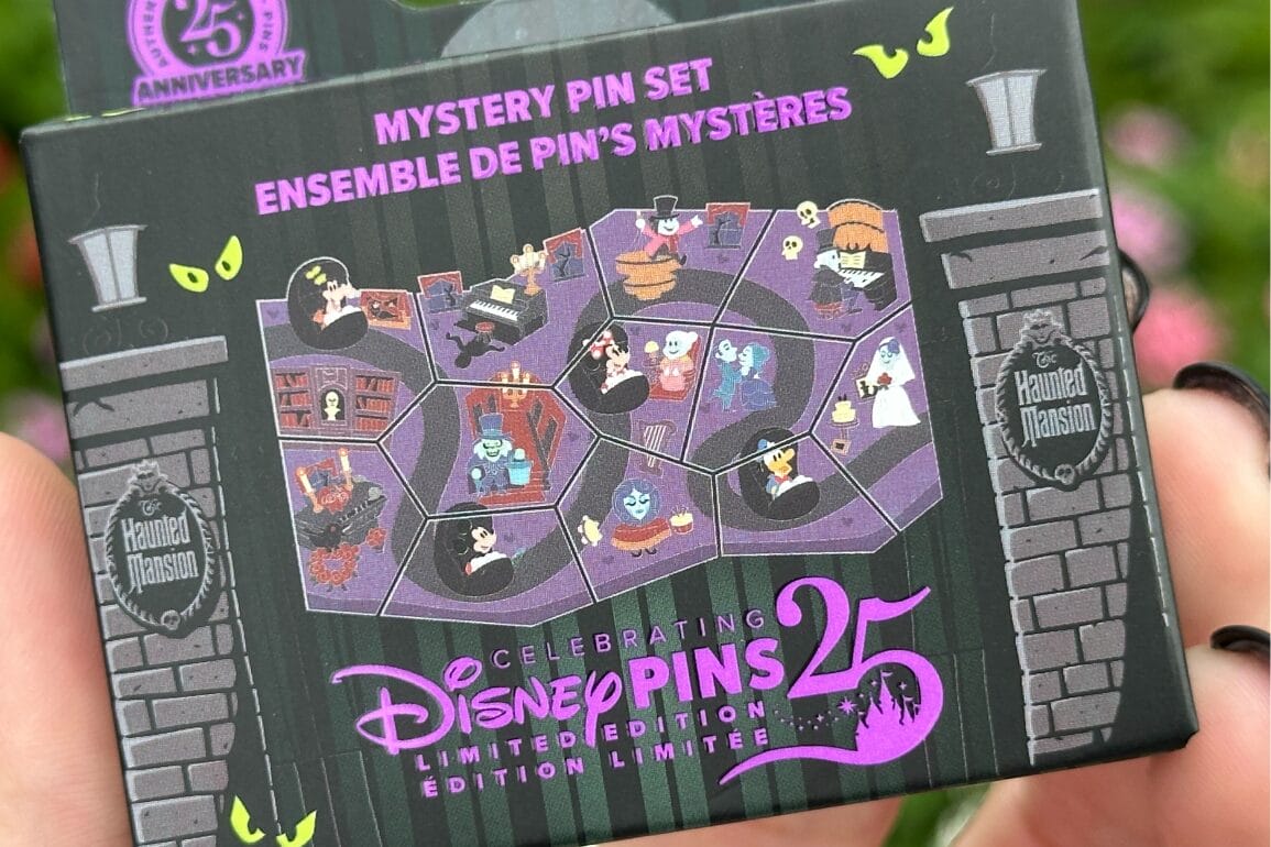 Person holding a Disney Haunted Mansion 25th Anniversary pin set box featuring cartoon ghost characters and Stitch.