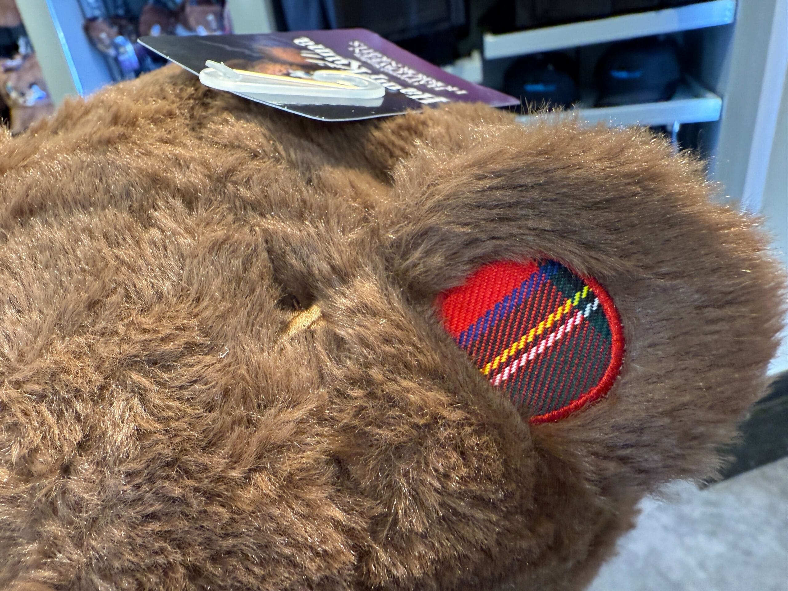 Close-up of a HamiKuma Merchandise bear's ear with red plaid fabric and tags; Universal Orlando Resort exclusive.