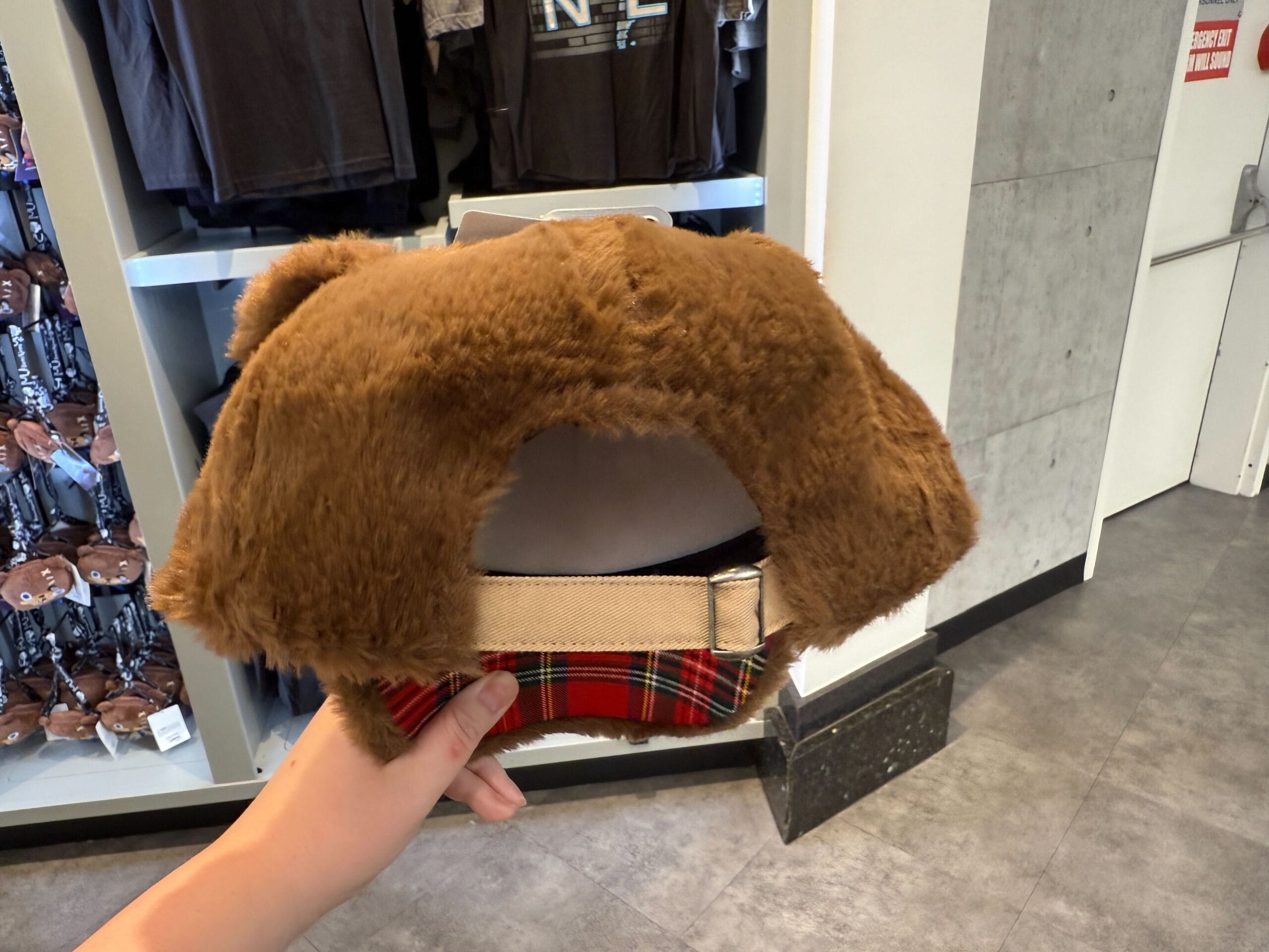 A hand holds a fuzzy brown bear hat with tartan trim, exclusive HamiKuma merchandise at Universal Orlando Resort.