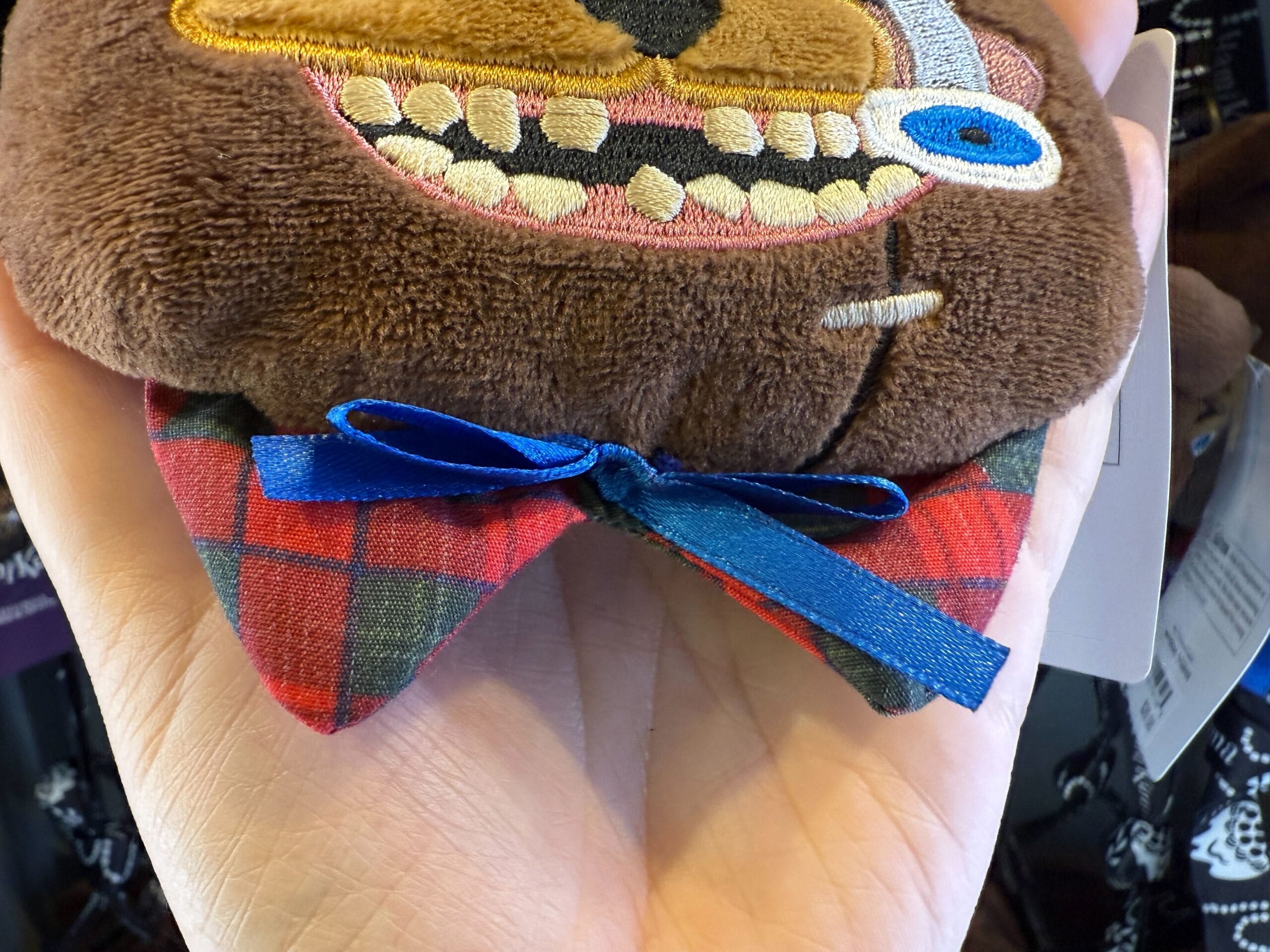 A hand holds a HamiKuma Merchandise bear face with a plaid bow tie at Universal Orlando Resort.