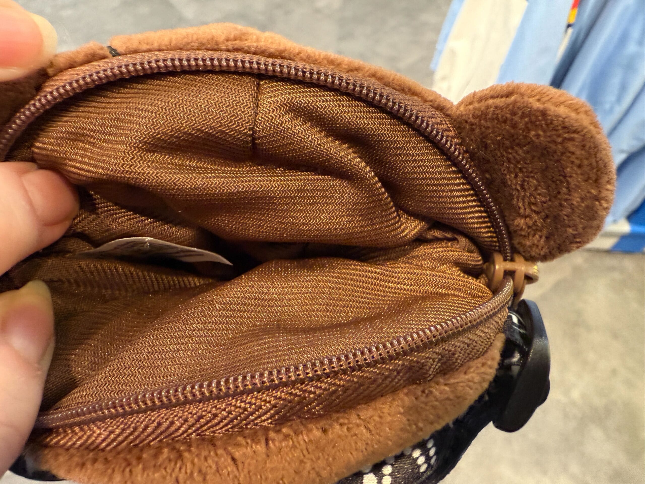 A hand holds open a HamiKuma Merchandise bear-shaped pouch at Universal Orlando Resort, revealing its empty interior.