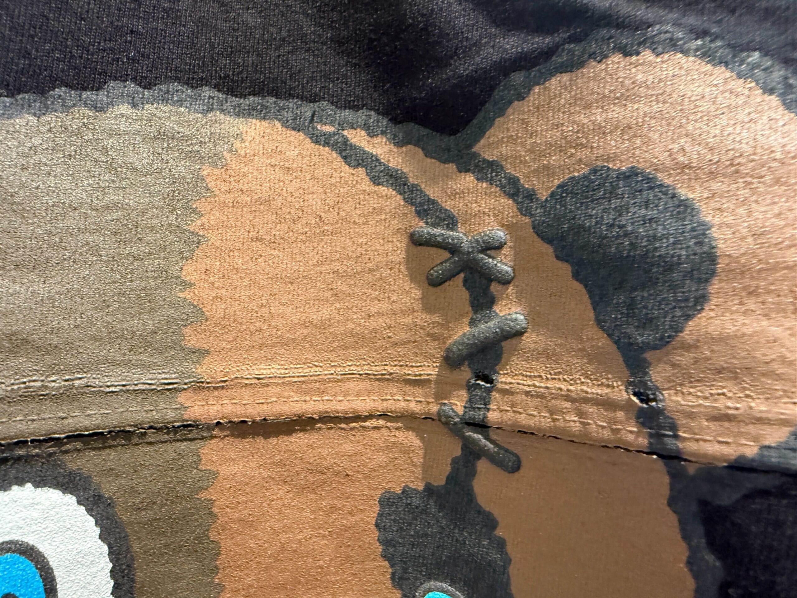 Close-up of a HamiKuma Merchandise cartoon bear print on fabric, with visible seam and decorative stitching across the middle.