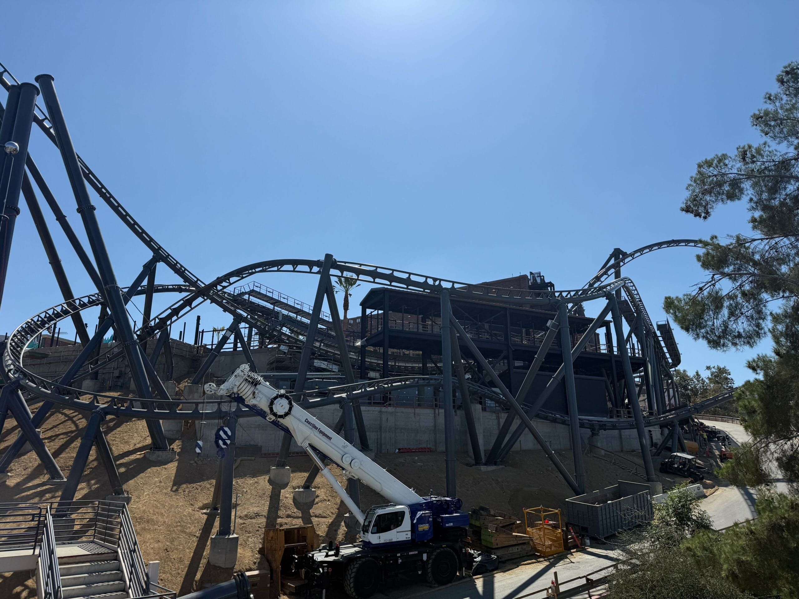 A Hollywood Drift roller coaster under construction with cranes and materials beneath a clear blue sky.
