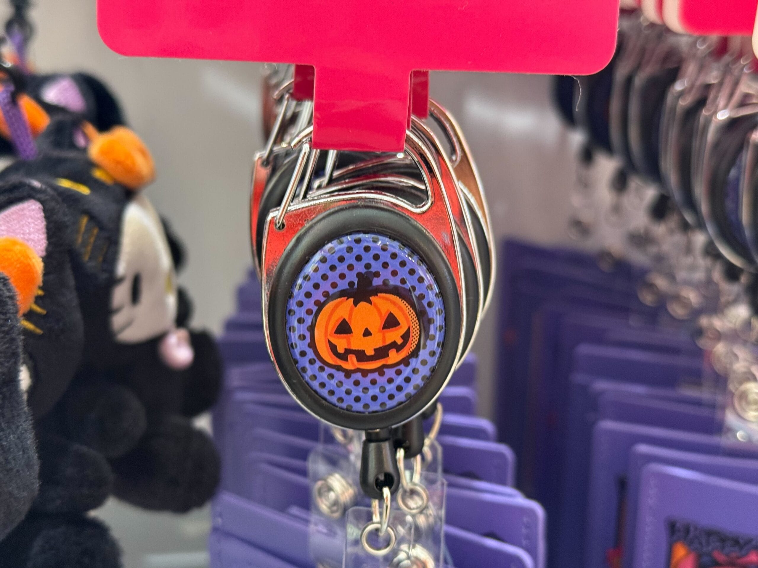 Close-up of Halloween merchandise: a retractable badge reel with a smiling jack-o'-lantern on a blue polka dot background.