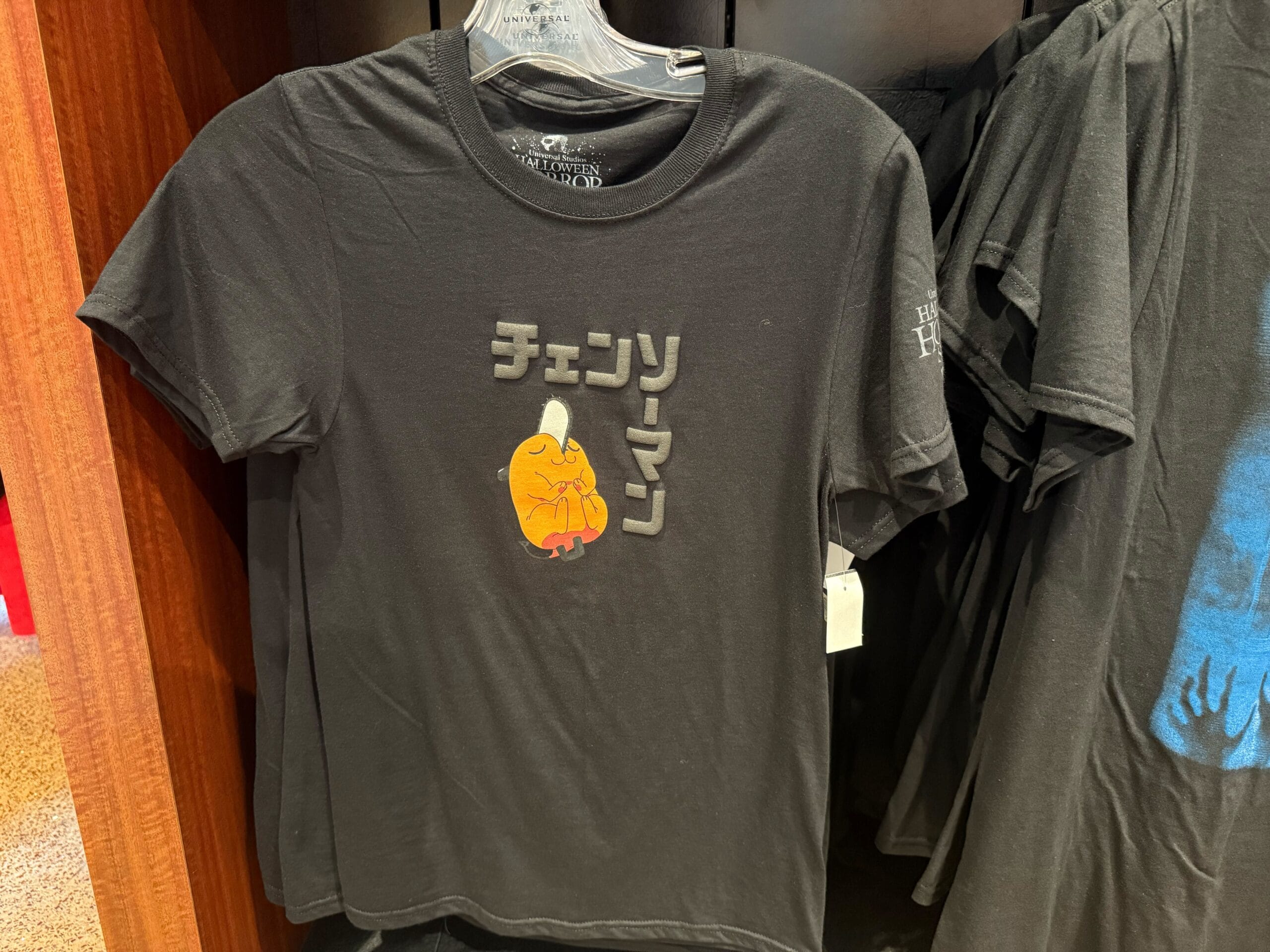Black t-shirt with a small orange cartoon character and Japanese text, exclusive HHN Merch 2025 at Universal Studios Hollywood.
