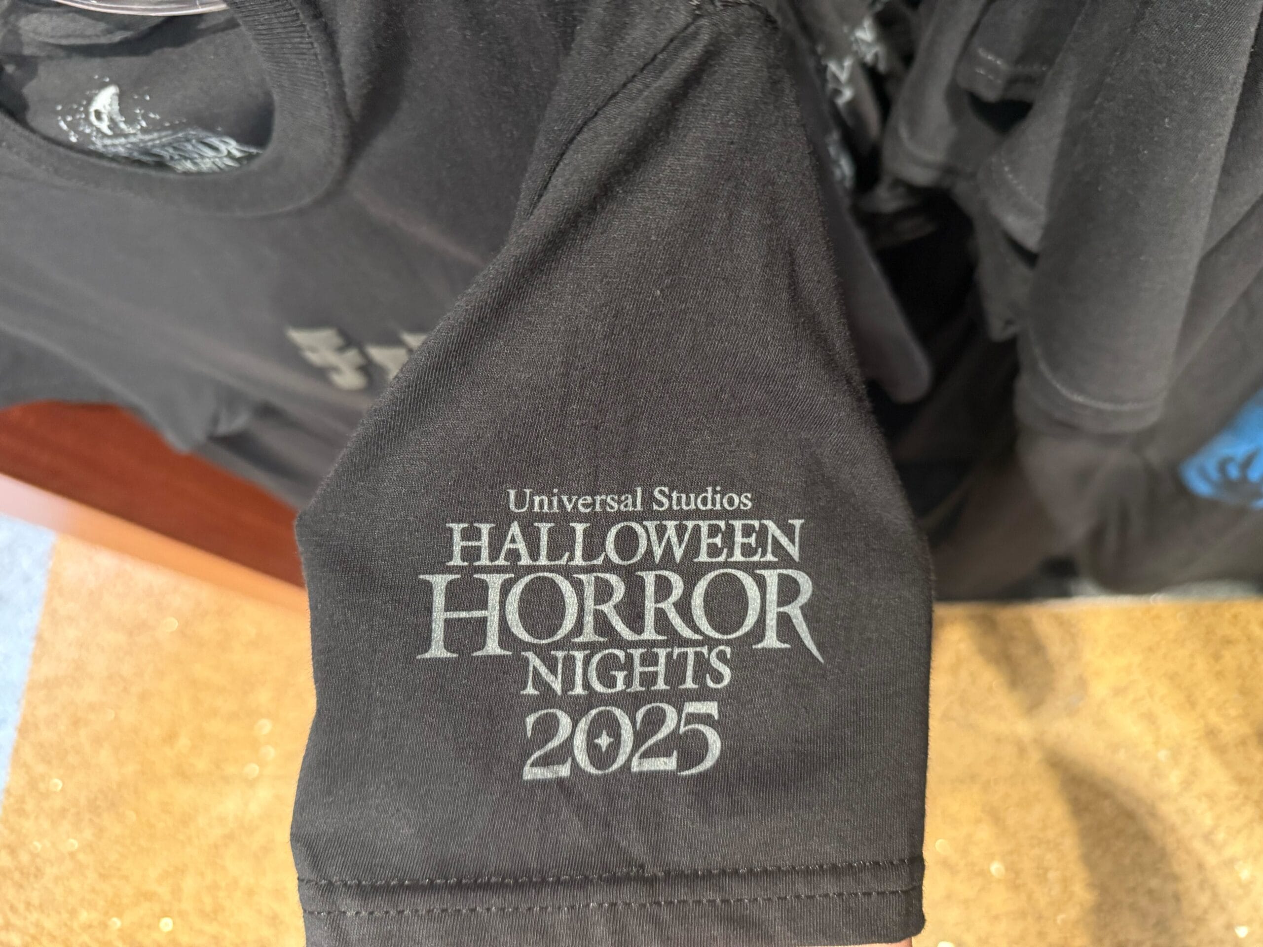 Black T-shirt with "Universal Studios Halloween Horror Nights 2025" sleeve print—exclusive HHN Merch 2025.