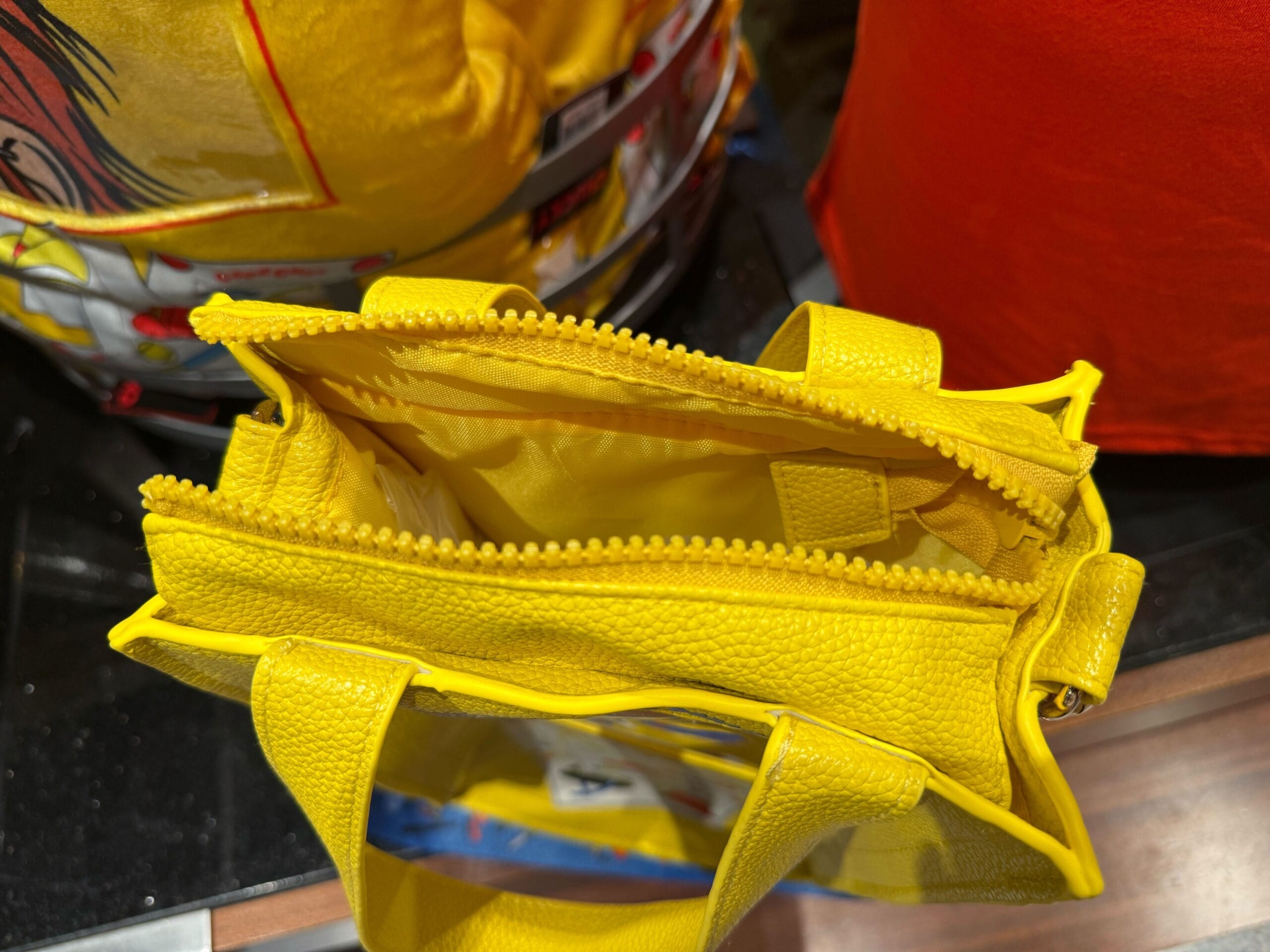 A small yellow zippered handbag, perfect for HHN Merch 2025, sits empty on a black surface.
