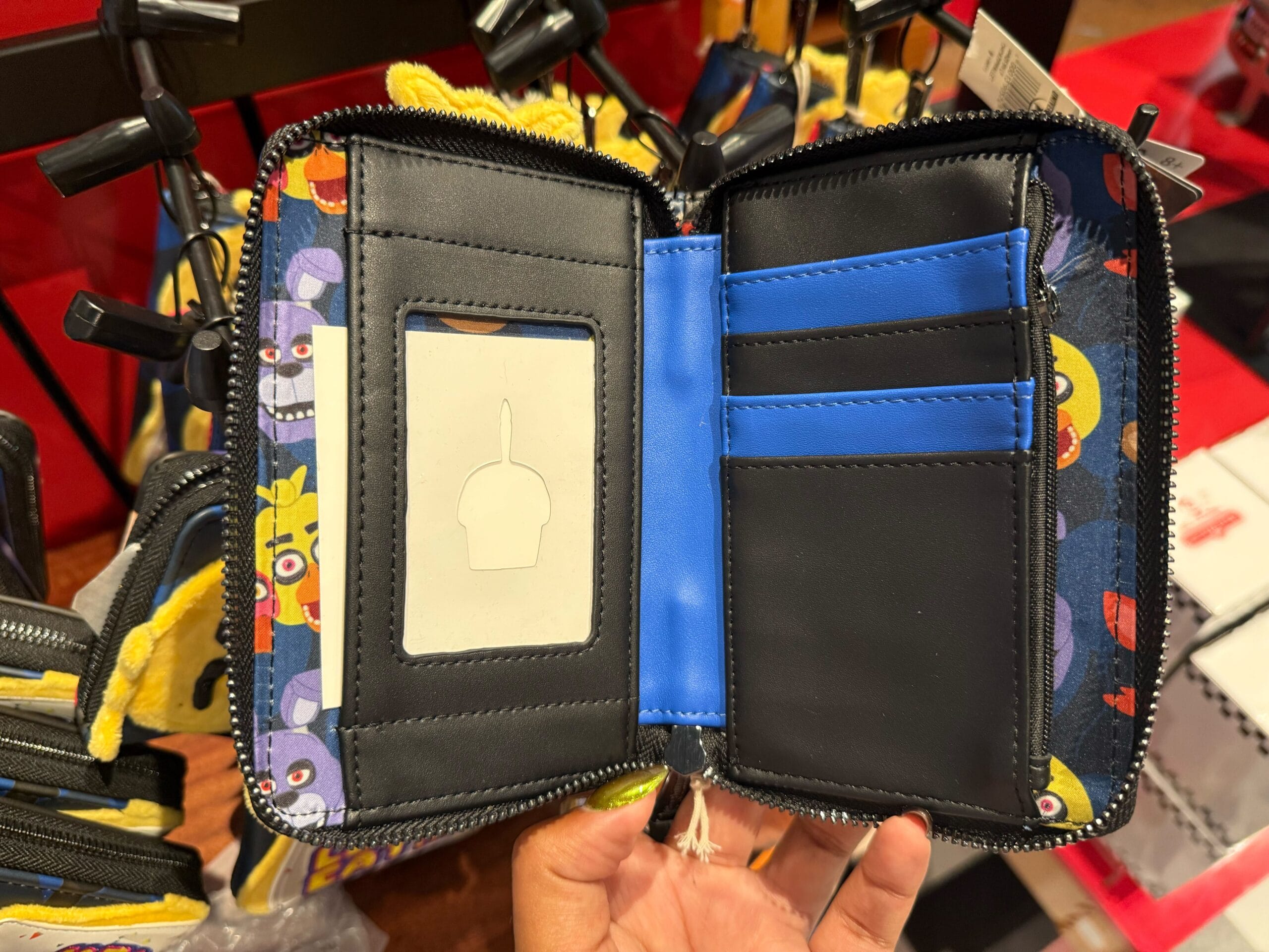 A hand holds open a wallet with blue slots and cartoon faces, inspired by Halloween Horror Nights Merchandise.