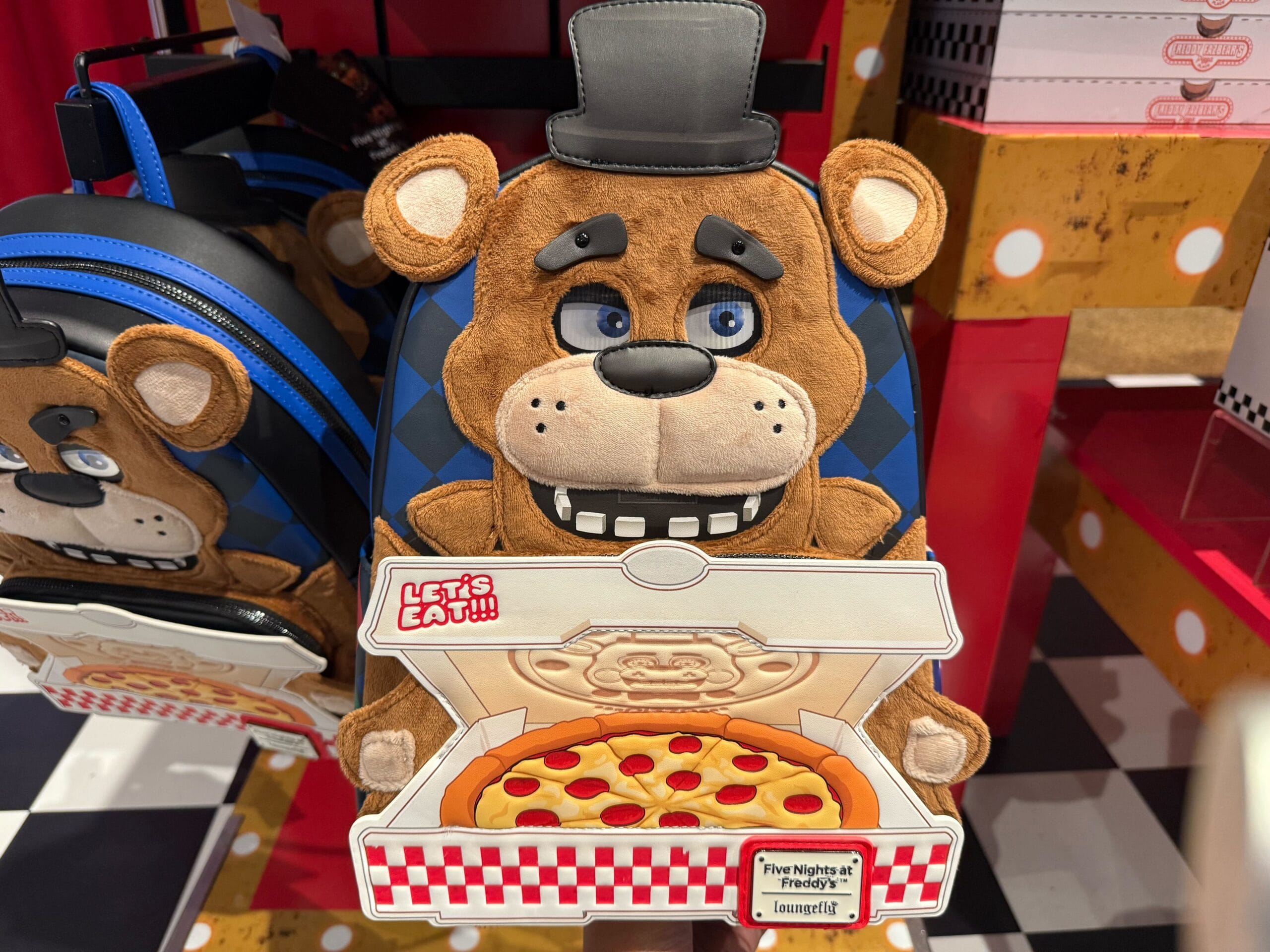 A plush Freddy Fazbear backpack with a "Let's Eat!" pizza box, part of the HHN Merch 2025 at Universal Studios Hollywood.
