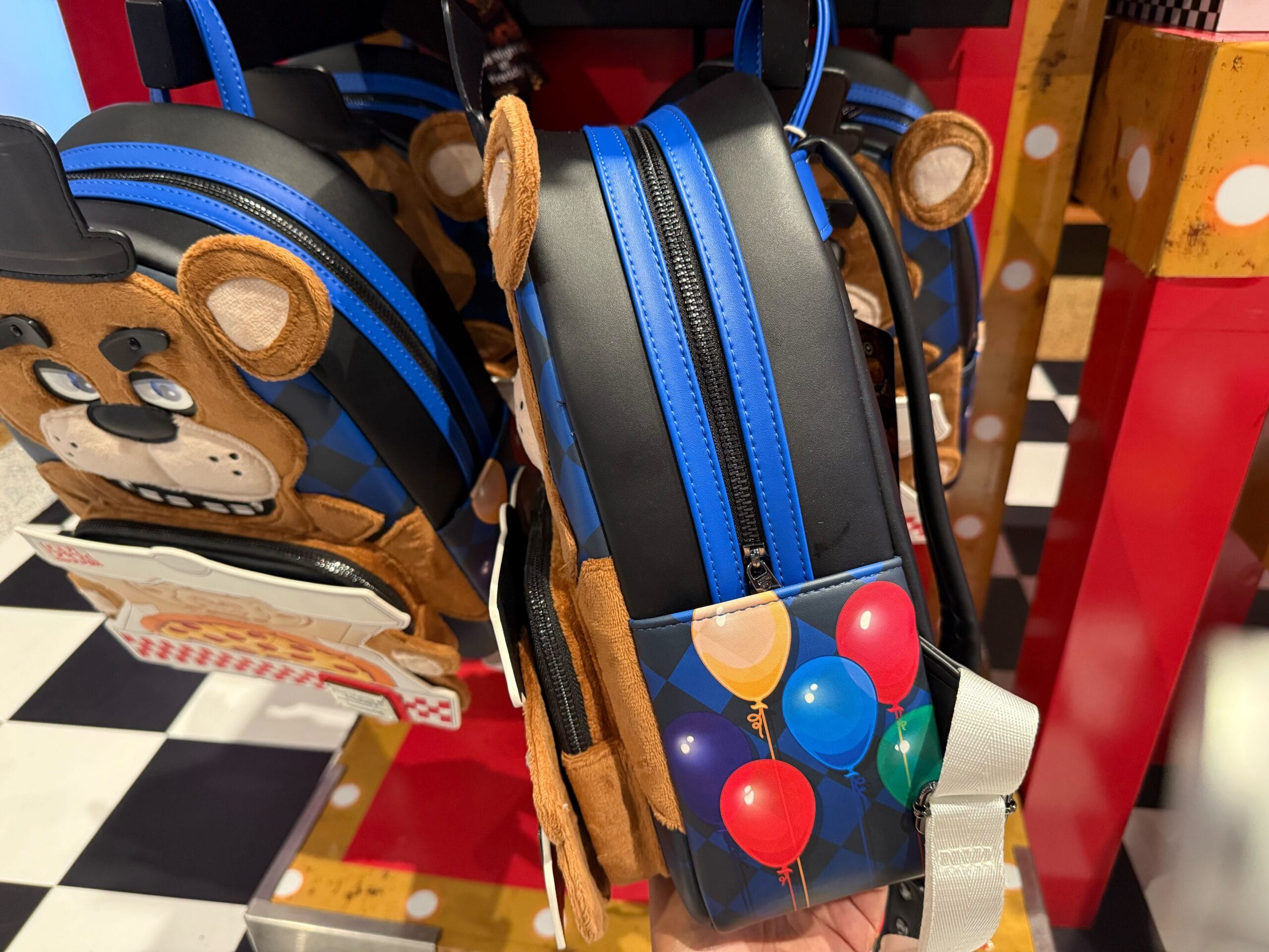 A backpack with colorful balloons sits beside bear-faced bags, part of the HHN Merch 2025 at Universal Studios Hollywood.