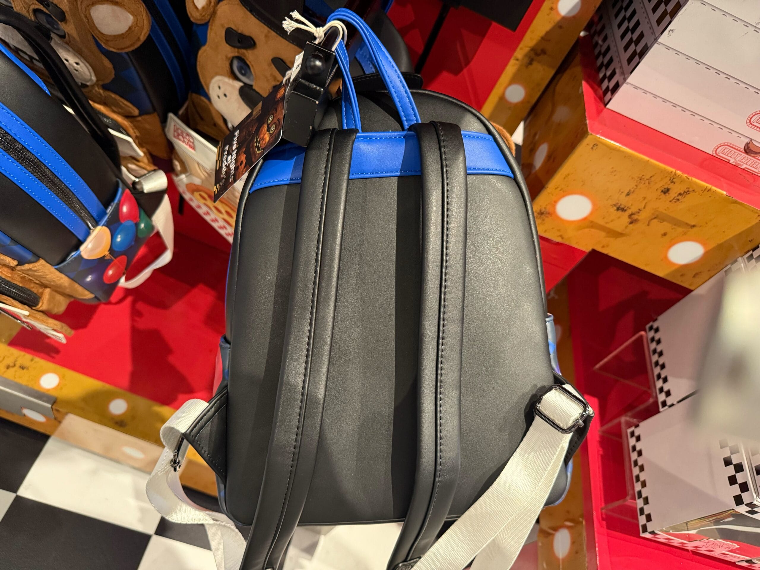 A black and blue backpack with white straps hangs in a store among Universal Studios Hollywood HHN Merch 2025.
