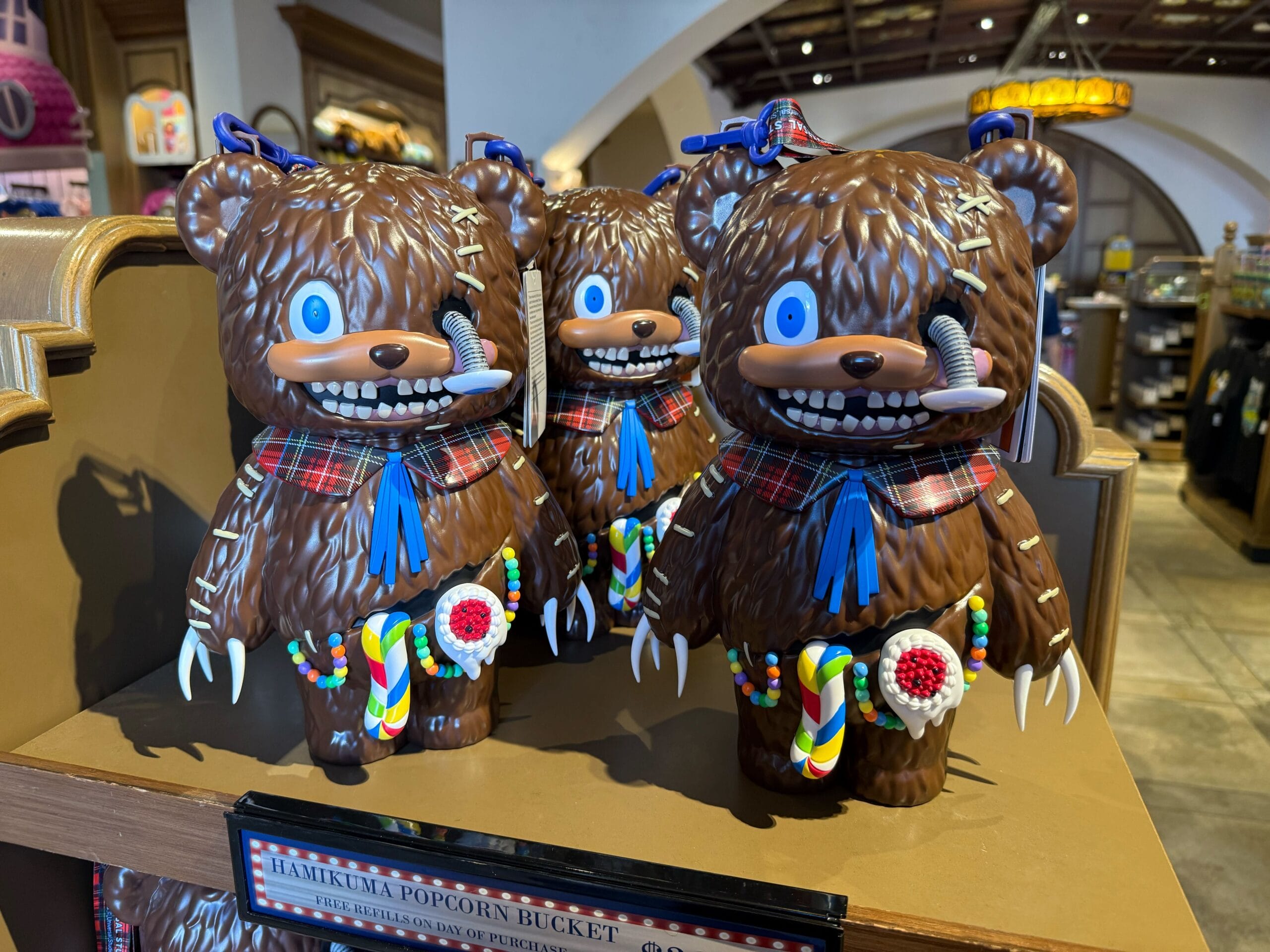 Three brown bear-shaped popcorn buckets, part of Universal Studios Hollywood HHN Merch 2025, are on display.
