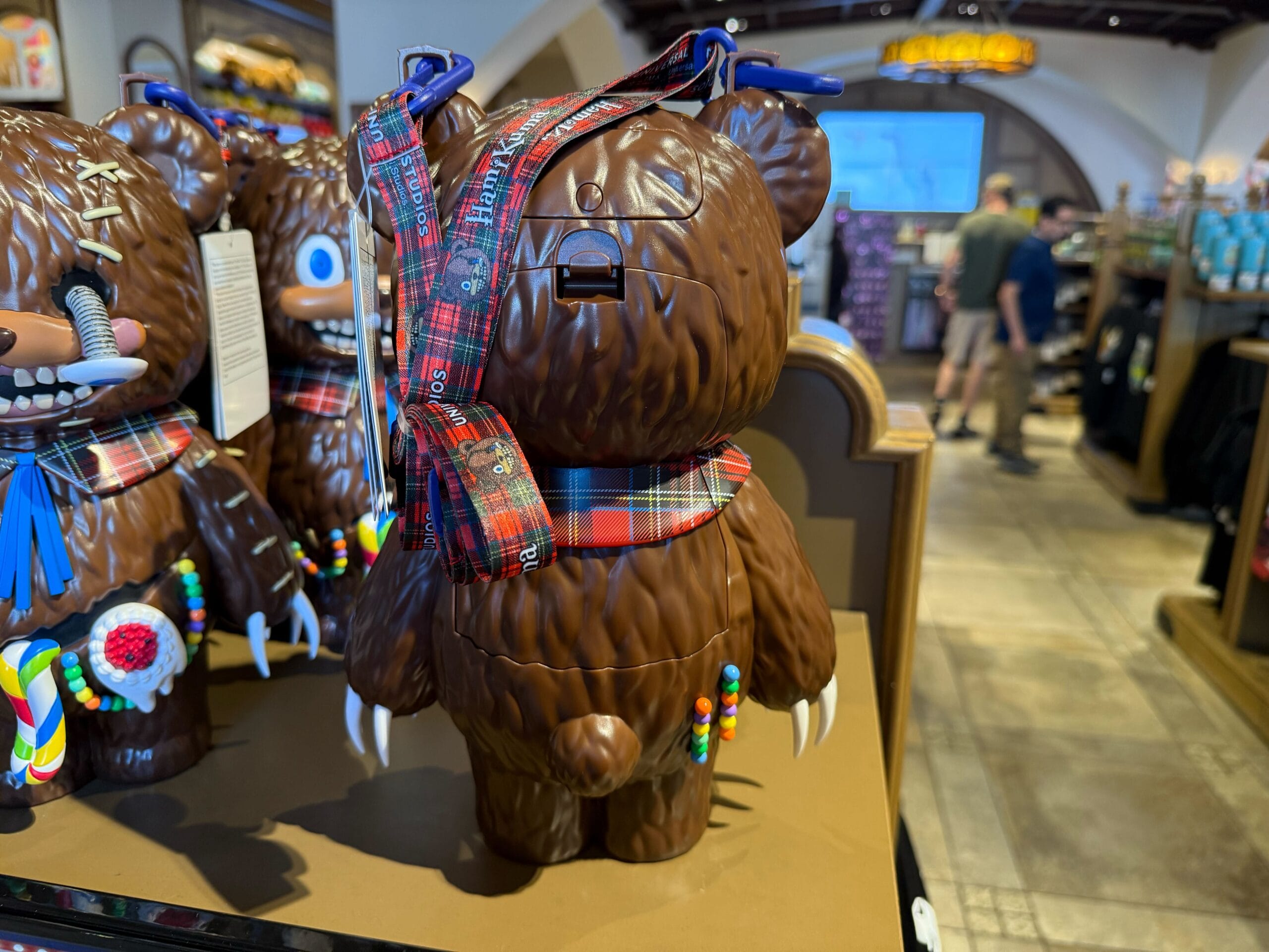 A bear-shaped figure with a plaid sash stands on display among Universal Studios Hollywood Halloween Horror Nights merchandise.