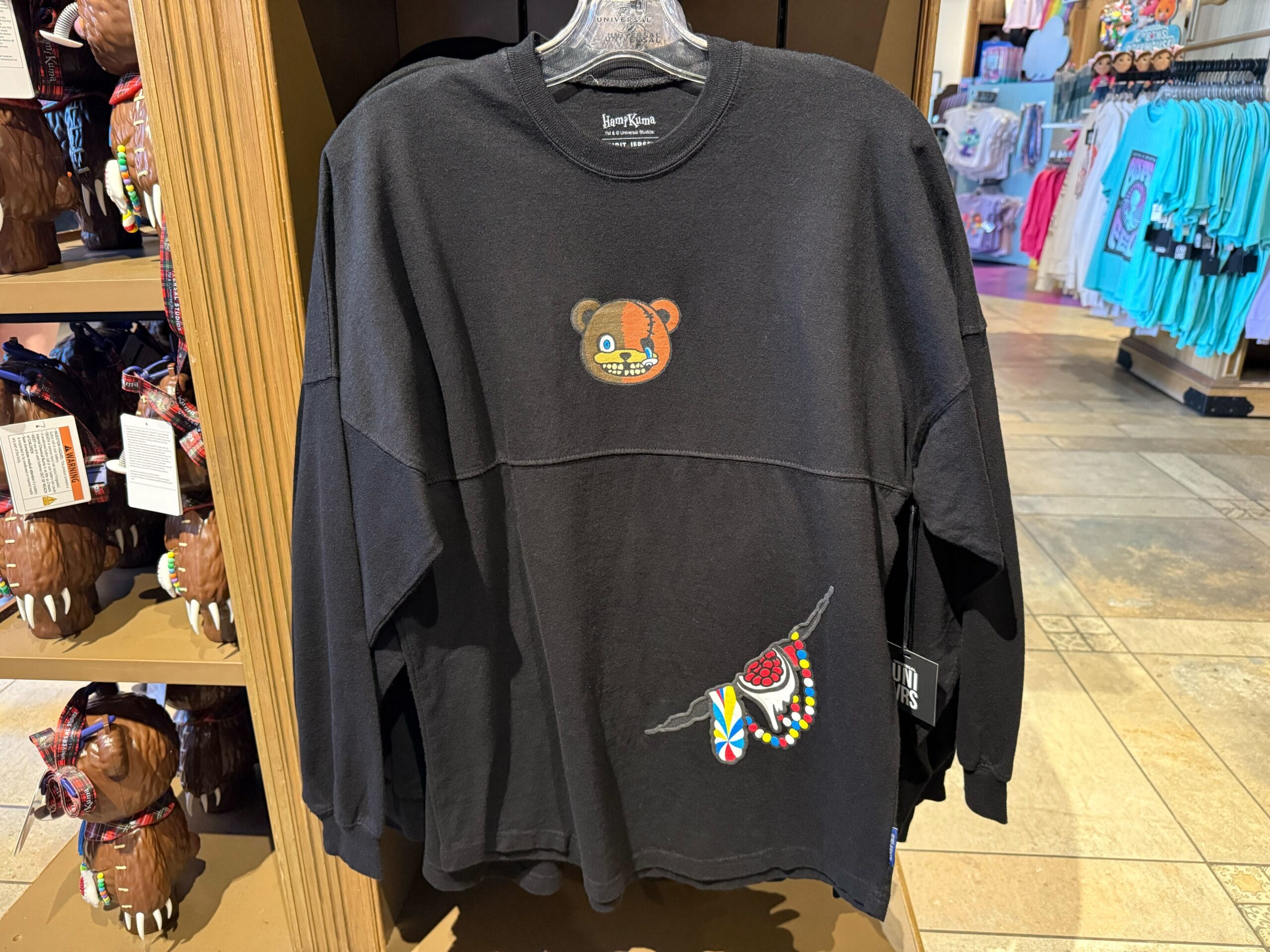 Black long-sleeve shirt with a bear face and beaded heart wings, part of HHN Merch 2025 at Universal Studios Hollywood.