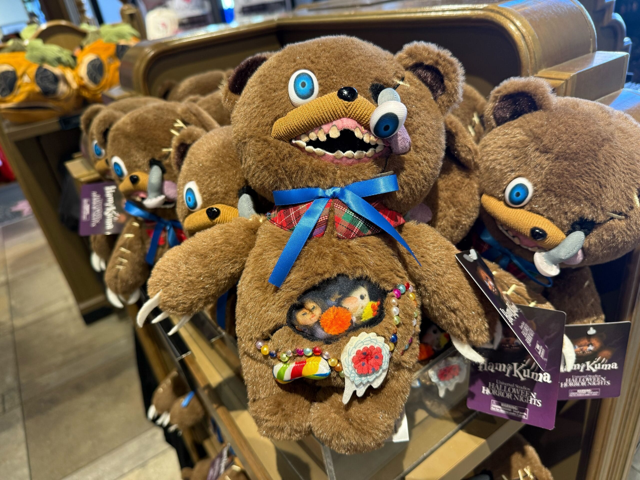 A display of quirky brown teddy bear plush toys inspired by Halloween Horror Nights with colorful, spooky belly decorations.