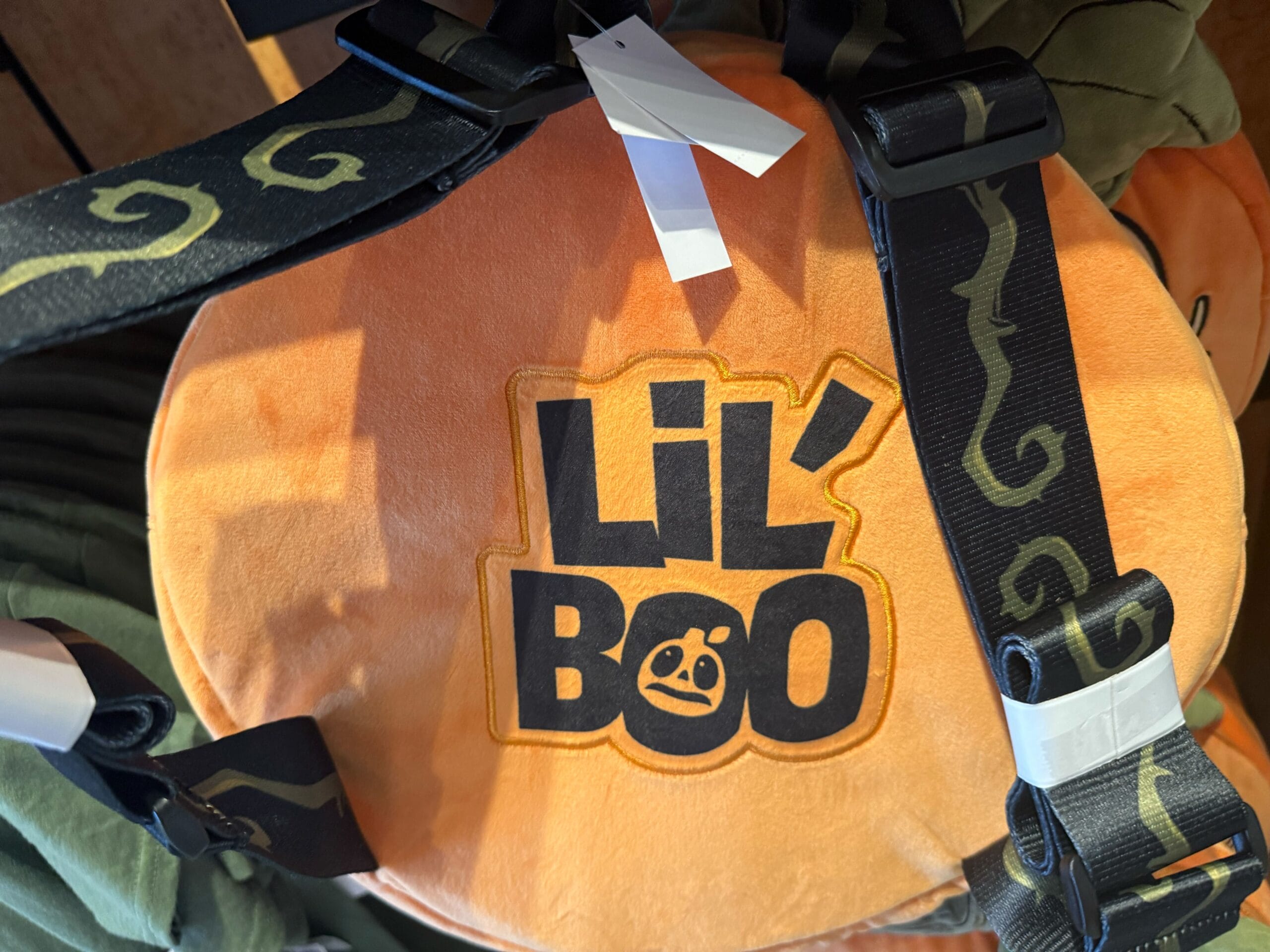 Close-up of an orange plush labeled "LIL' BOO," a cute addition to Halloween Horror Nights Merchandise, with green-detailed straps.