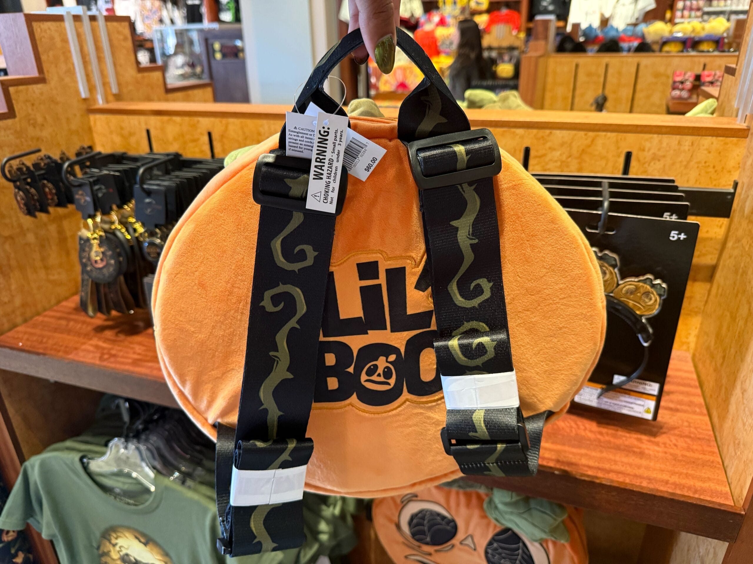 A plush orange pumpkin-shaped backpack with "Lil Boo" text, part of the Halloween Horror Nights Merch 2025 collection.