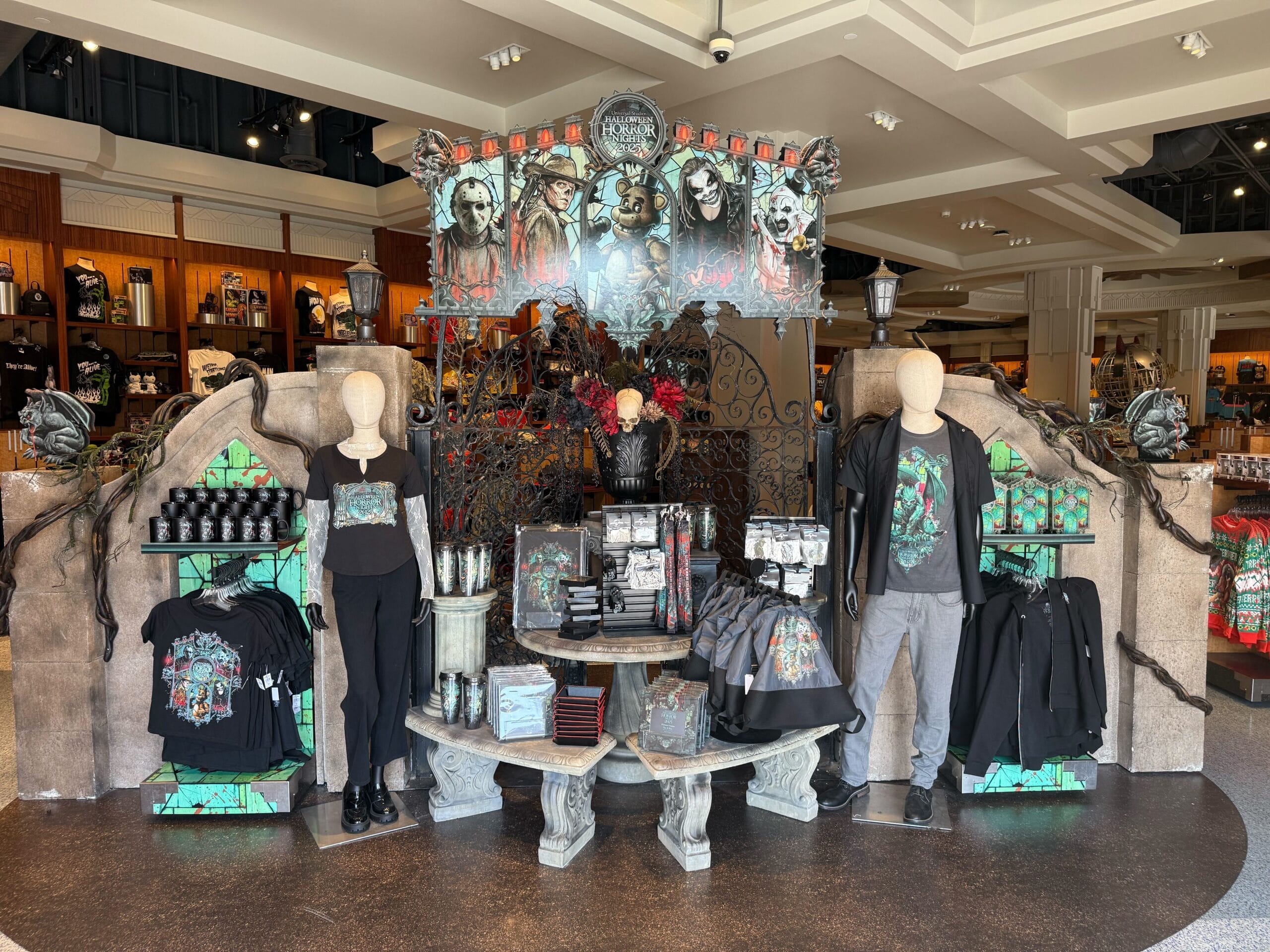 Store display with Haunted Mansion-themed merchandise, including shirts, cups, and bags, surrounded by spooky decorations.