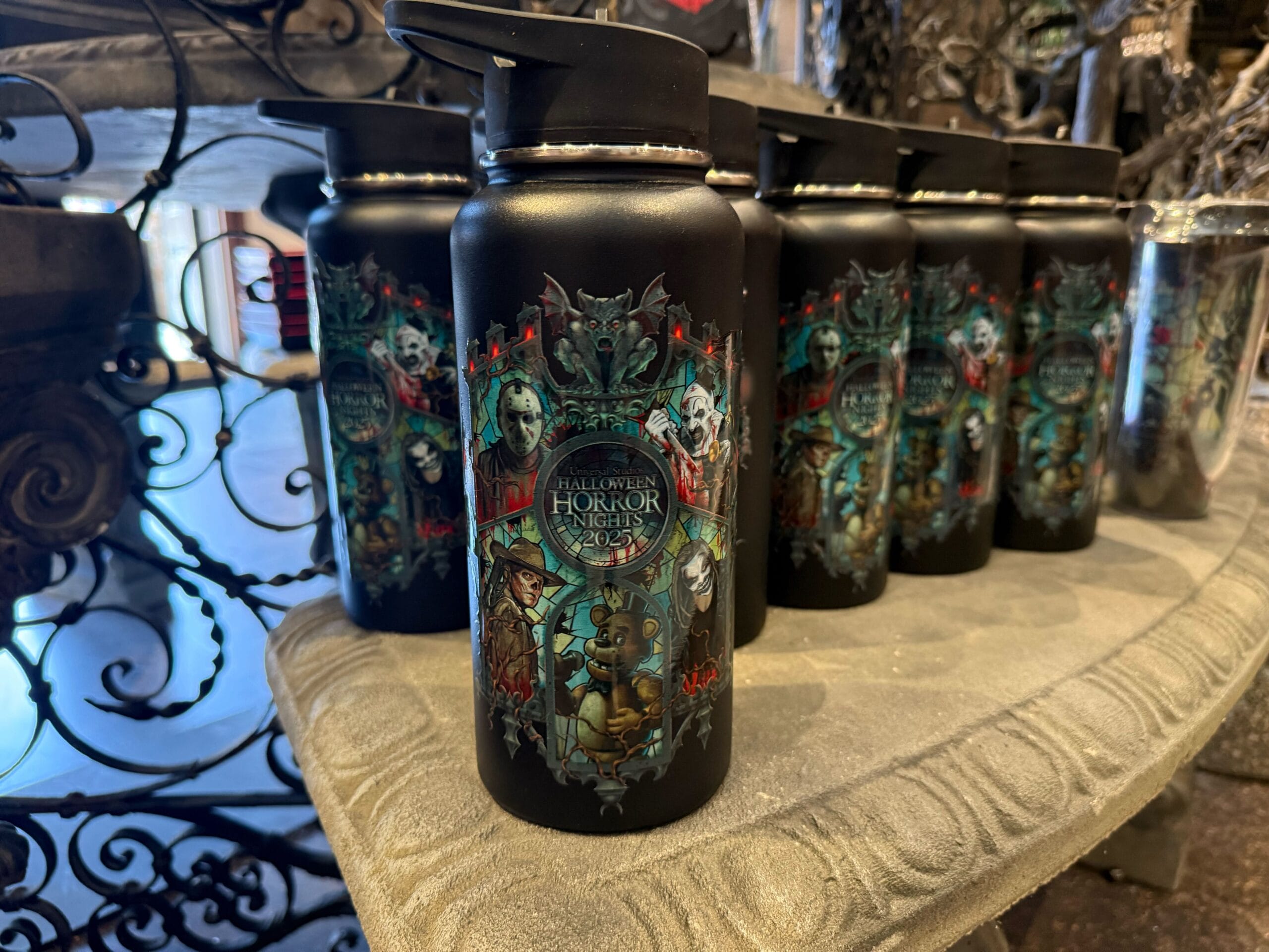 Black water bottles with colorful Halloween Horror Nights 2023 designs displayed on a stone-like shelf.